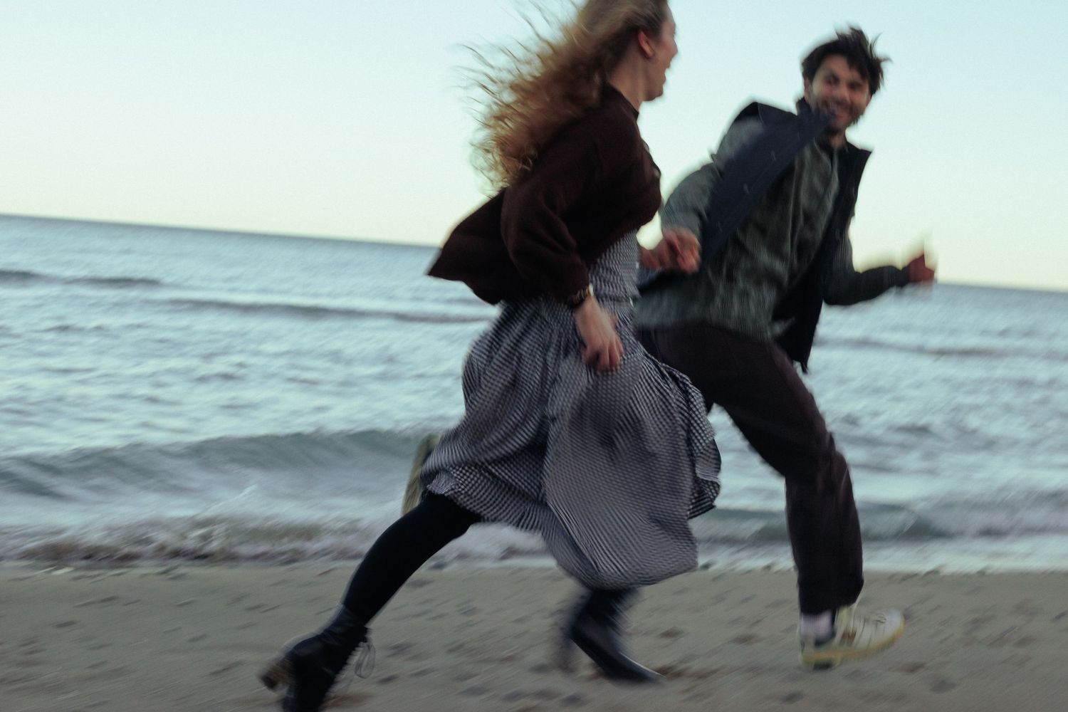 Playful couple dancing and jumping together on a beach.
