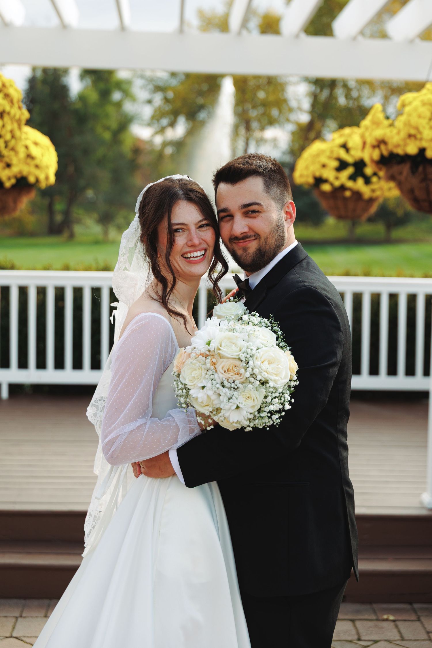 Newlyweds sharing romantic moments under a white pergola with yellow flowers.