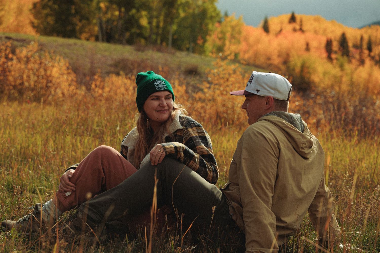 People relaxing in tall grass with mountain backdrop during fall season.