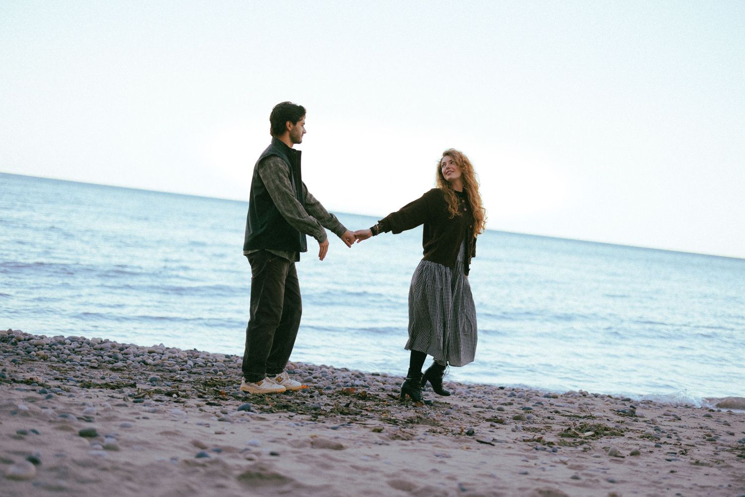 Couple holding hands while dancing on a beach at sunset.