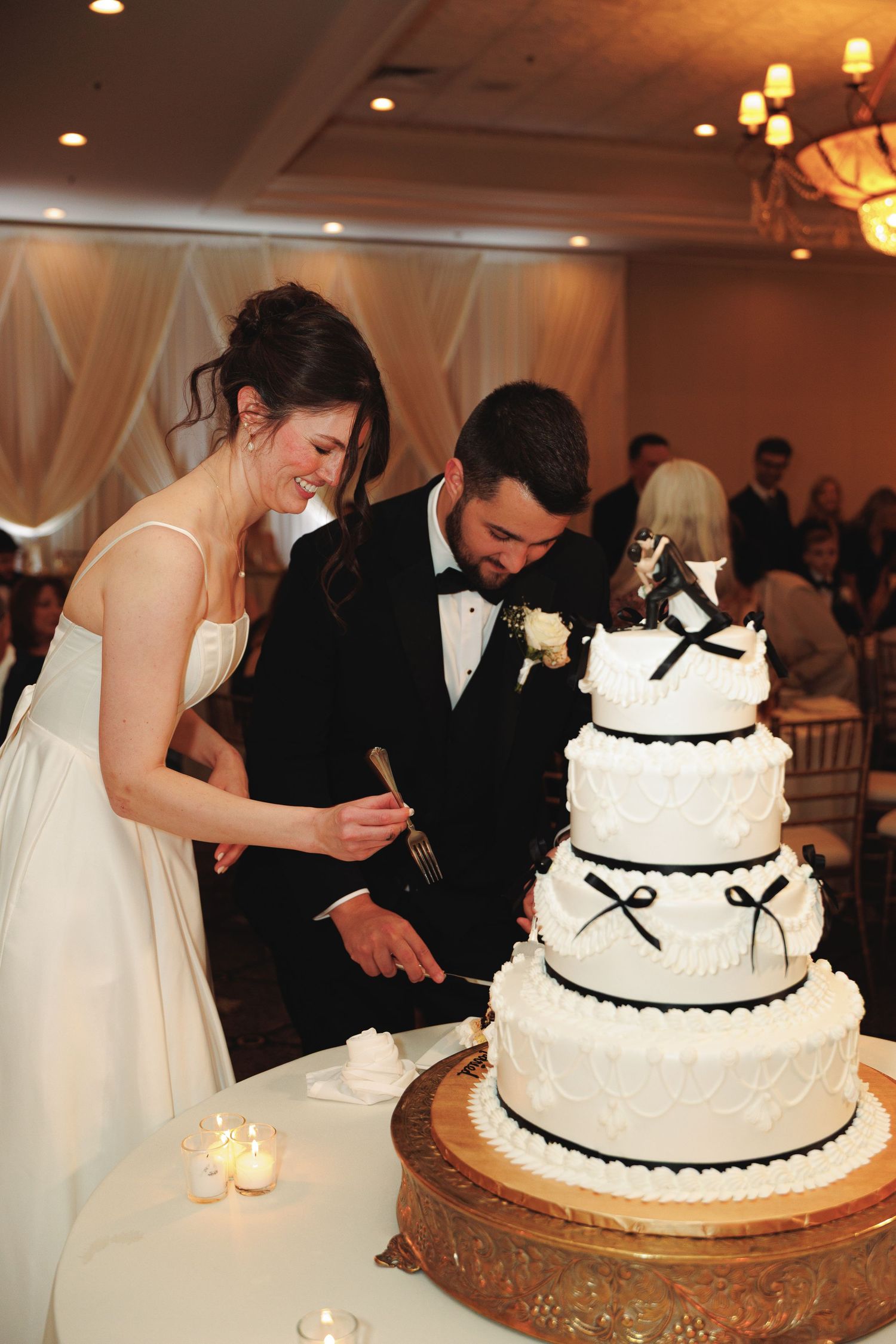Wedding couple cutting their elegant three-tiered white cake decorated with black trim.