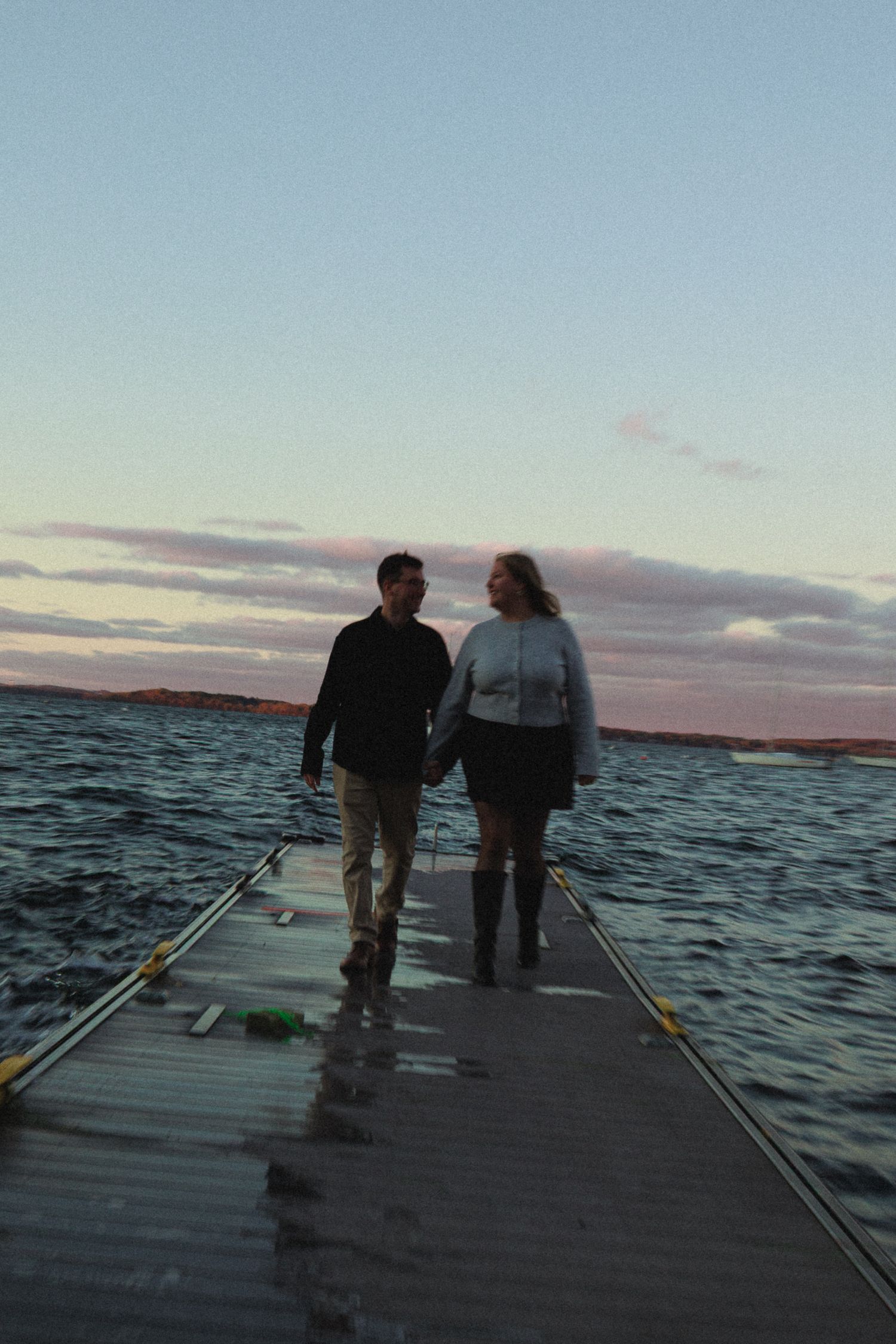 Two people standing on a dock overlooking choppy waters at sunset.