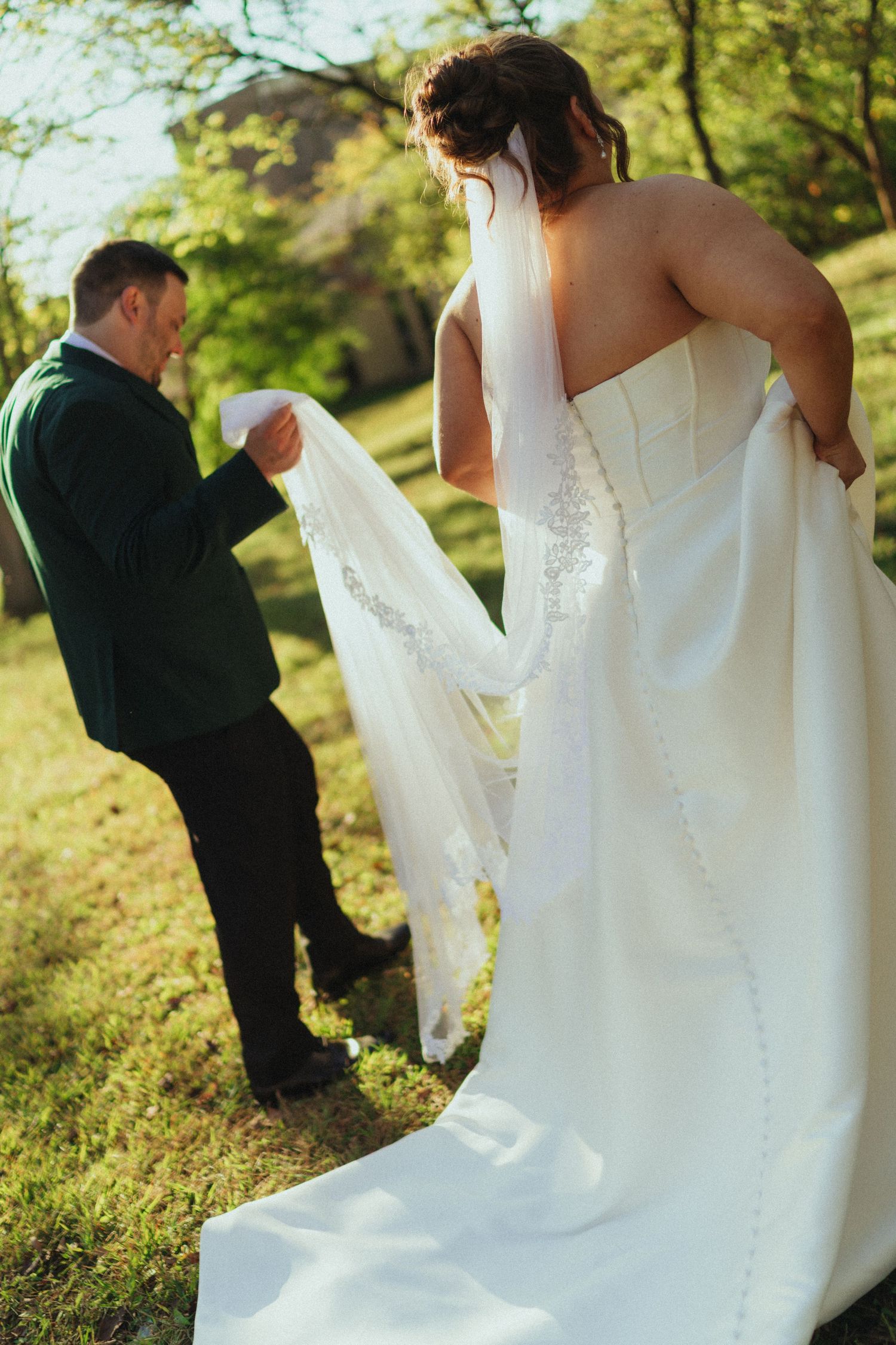 Couple in wedding attire posing together on a grassy hillside in natural sunlight.