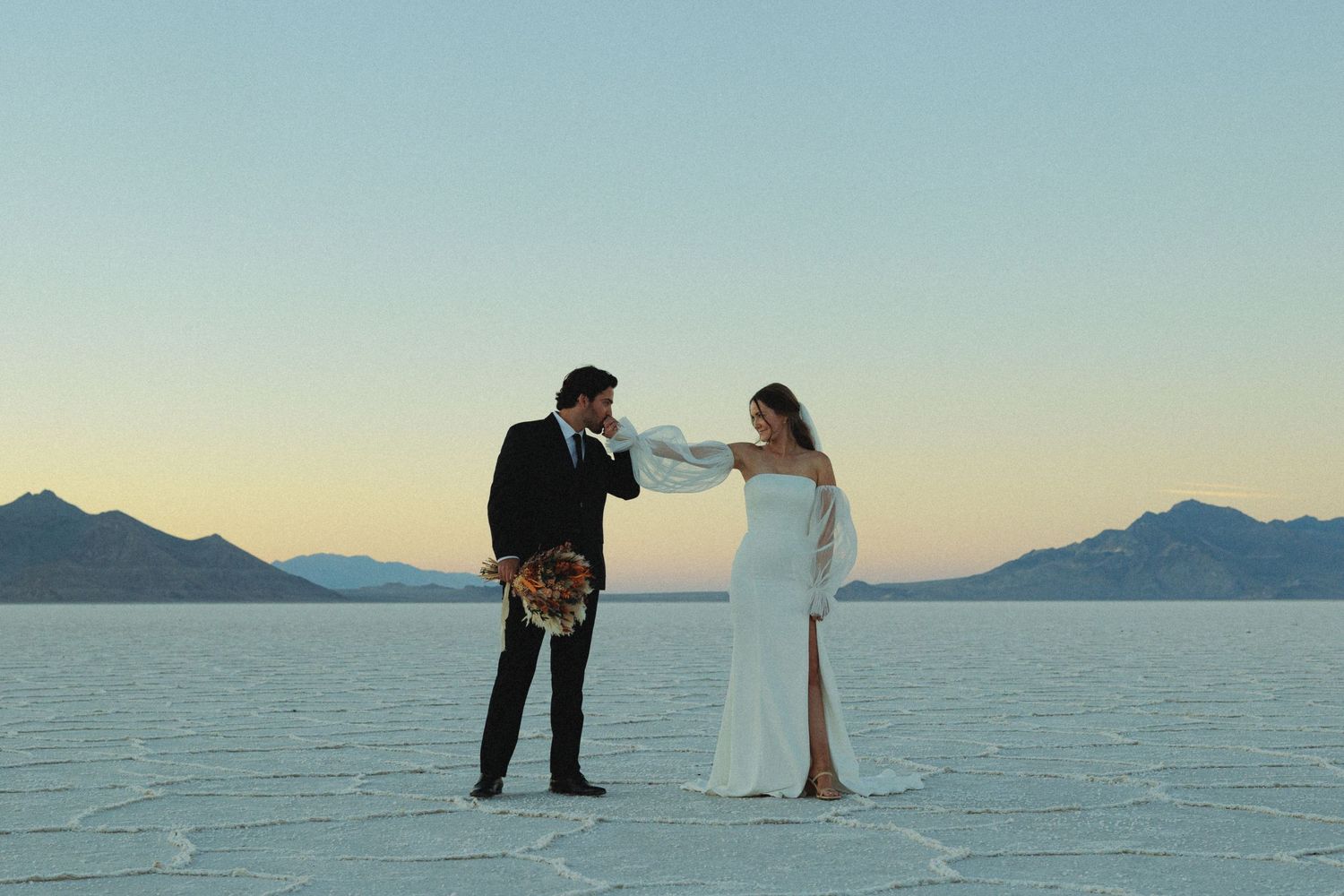 Wedding couple walks across expansive utah salt flats during golden hour.