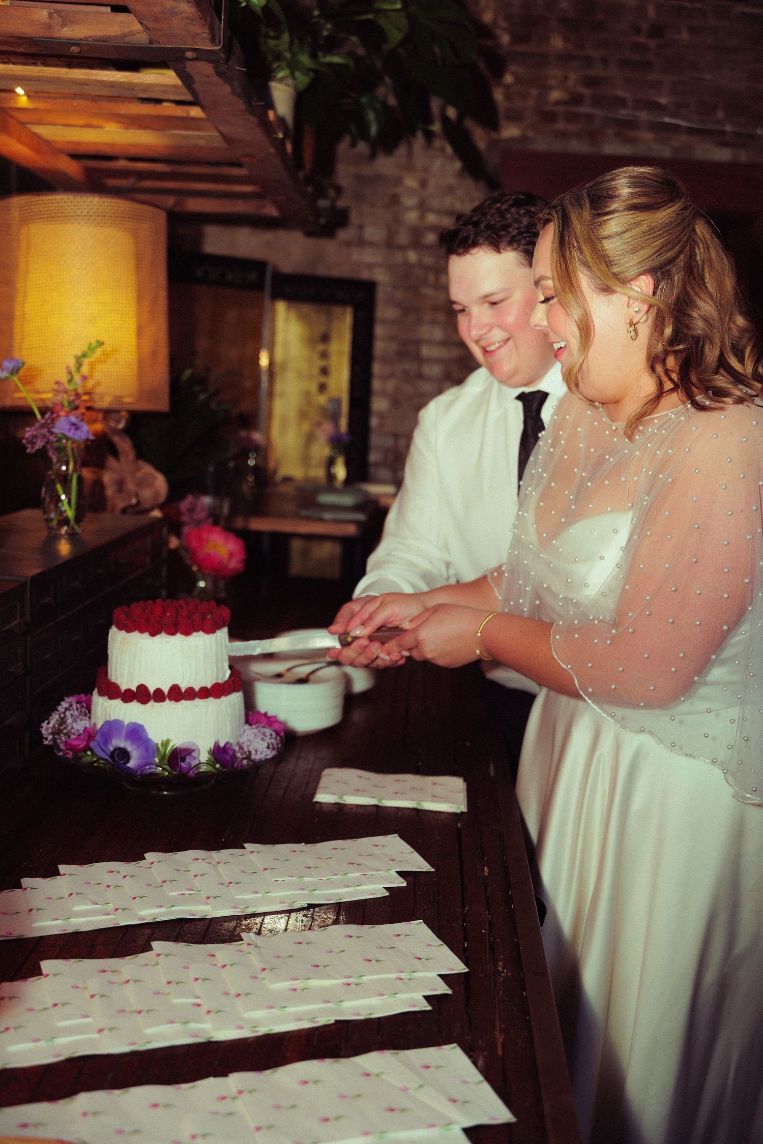 Wedding cake cutting ceremony in rustic brick venue with warm lighting.