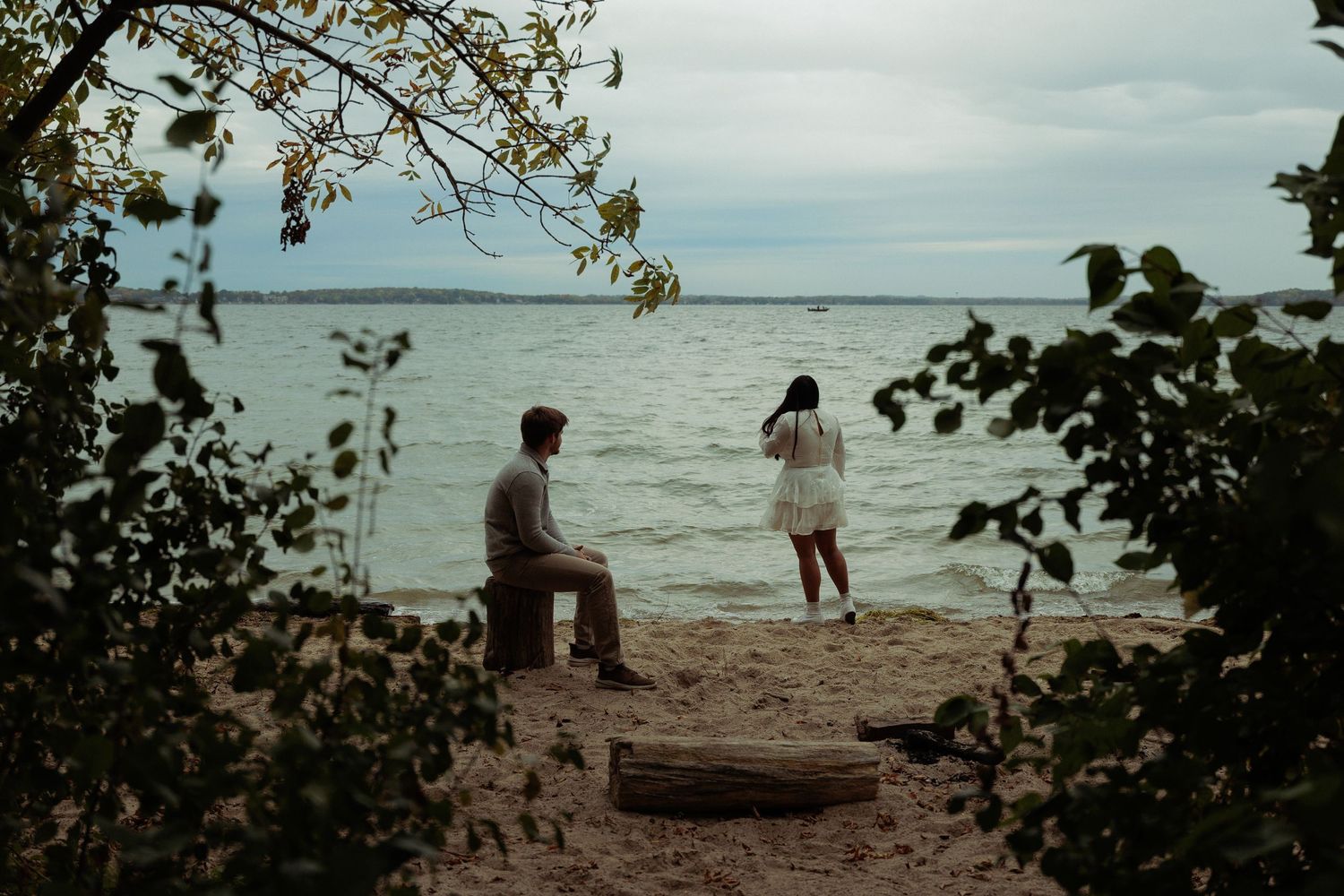 Two people enjoy a peaceful moment by the waterfront framed by tree branches.