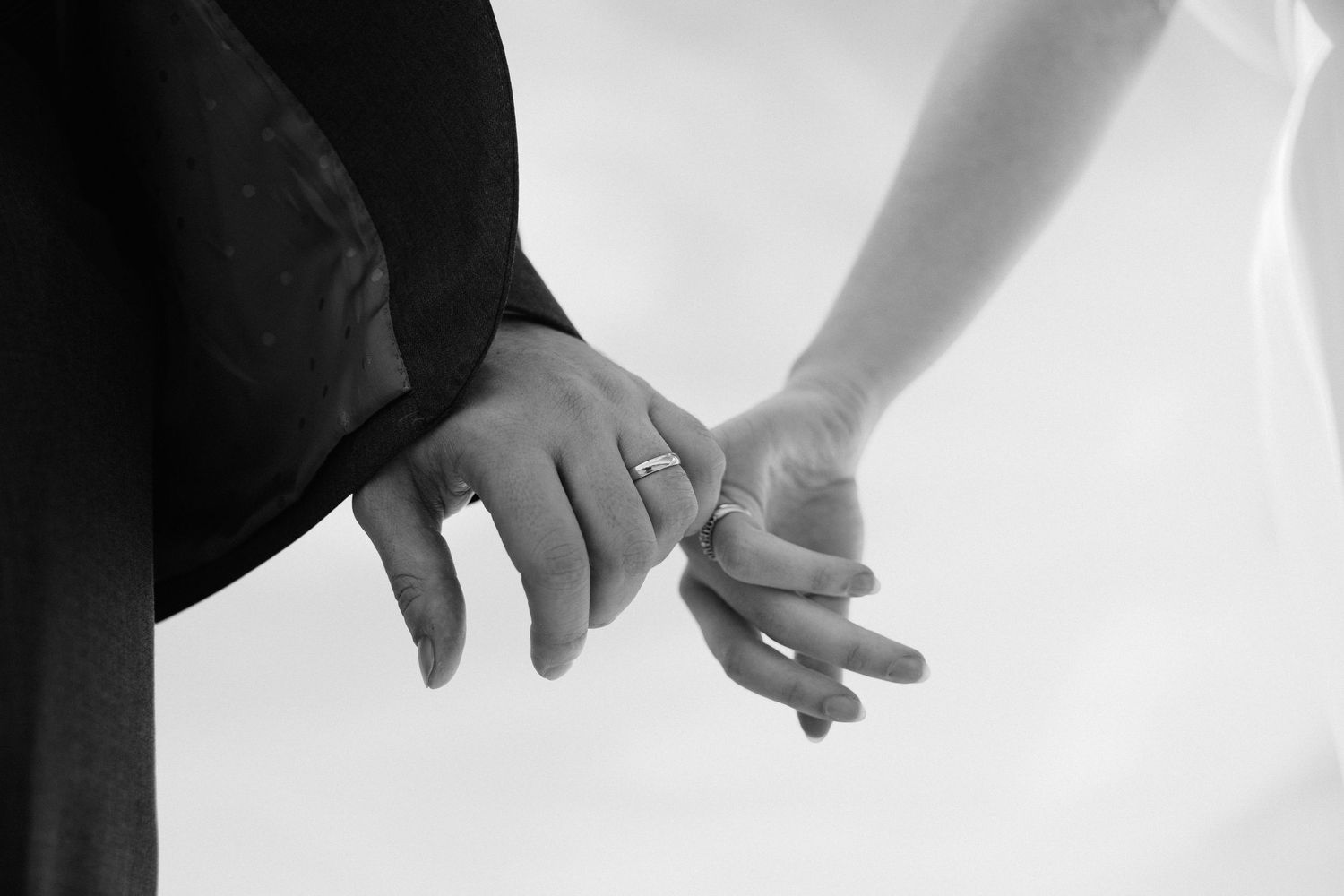 Black and white photo of a bride and groom holding hands, showcasing wedding rings during a romantic ceremony.
