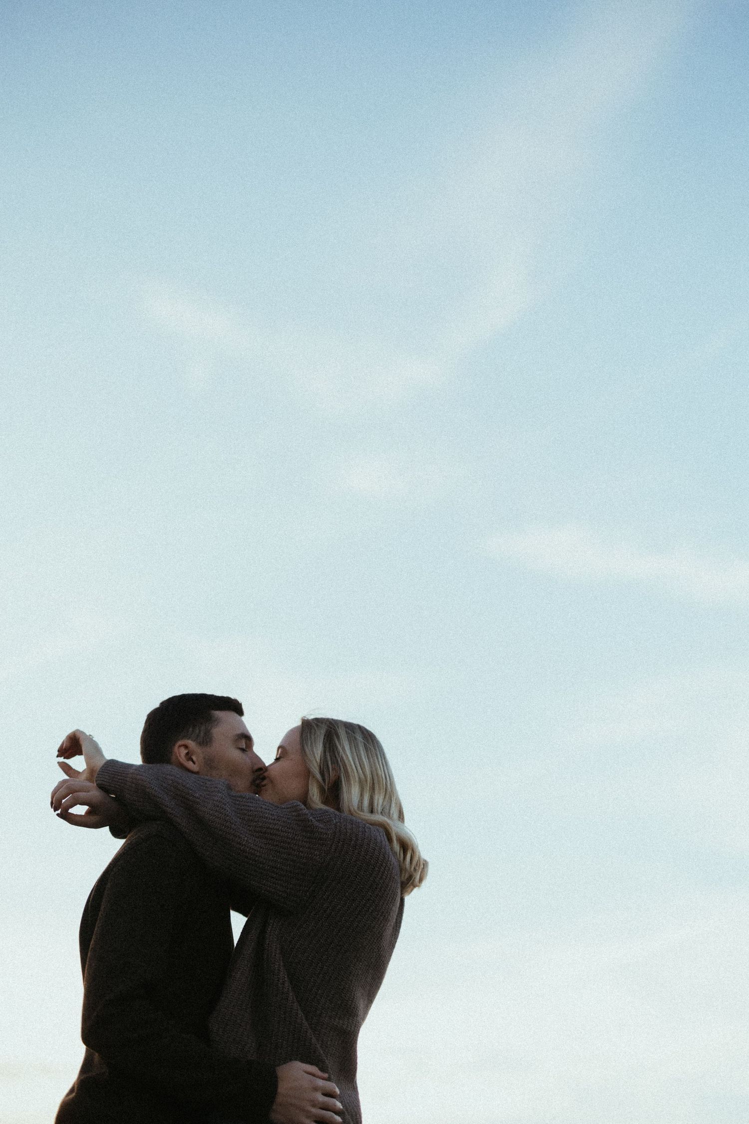 Couple sharing an intimate moment against a bright blue sky background.