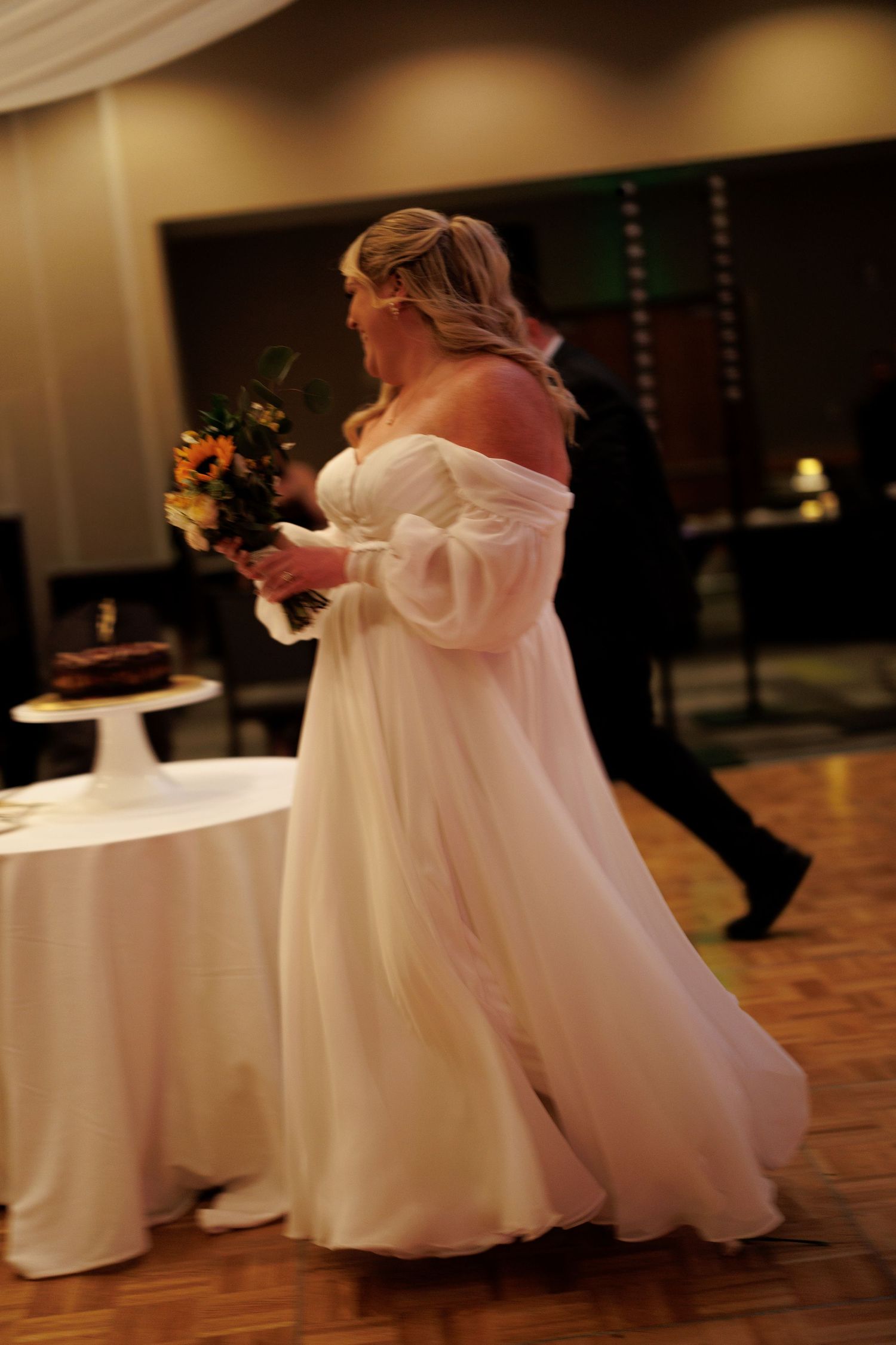 Bride in flowing white gown twirling on dance floor during wedding reception.