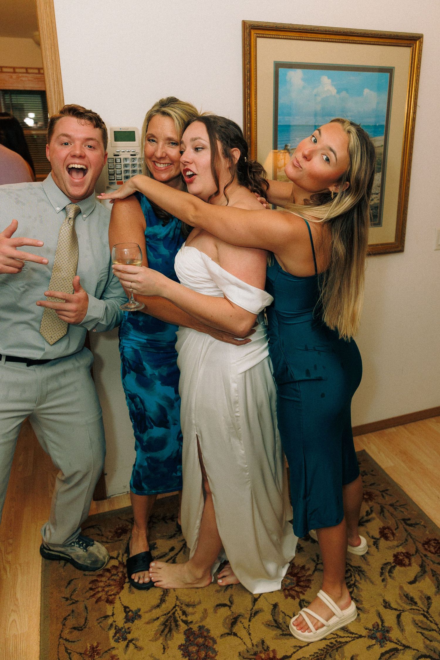 Wedding party members pose playfully in a room with framed artwork on the walls.