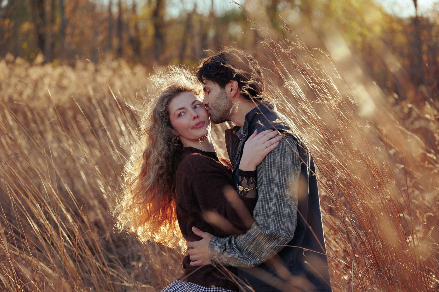 Romantic couple embracing in a golden field during sunset with warm autumn lighting.