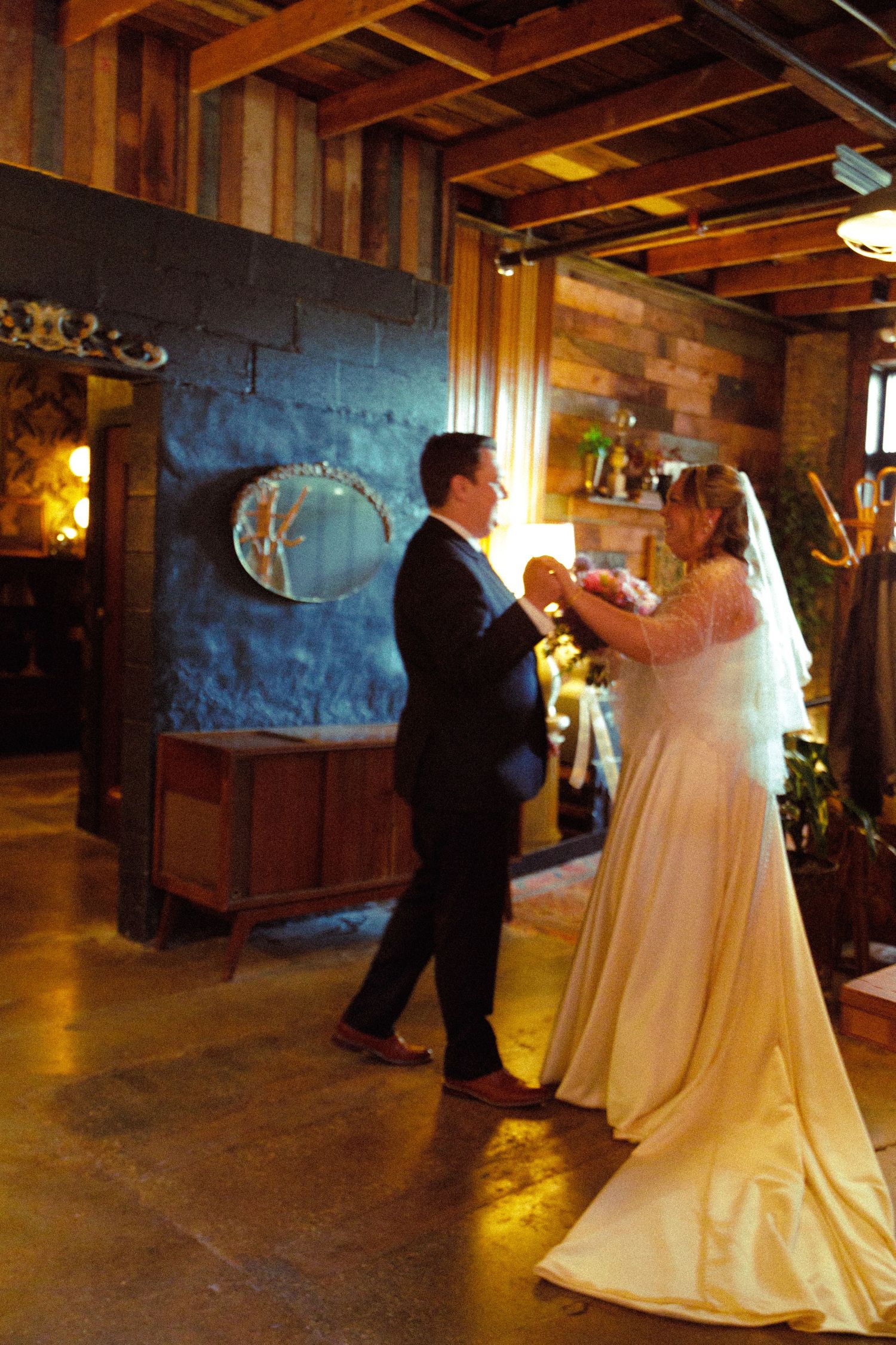 Couple dancing in a rustic venue with wooden beams and ambient lighting.