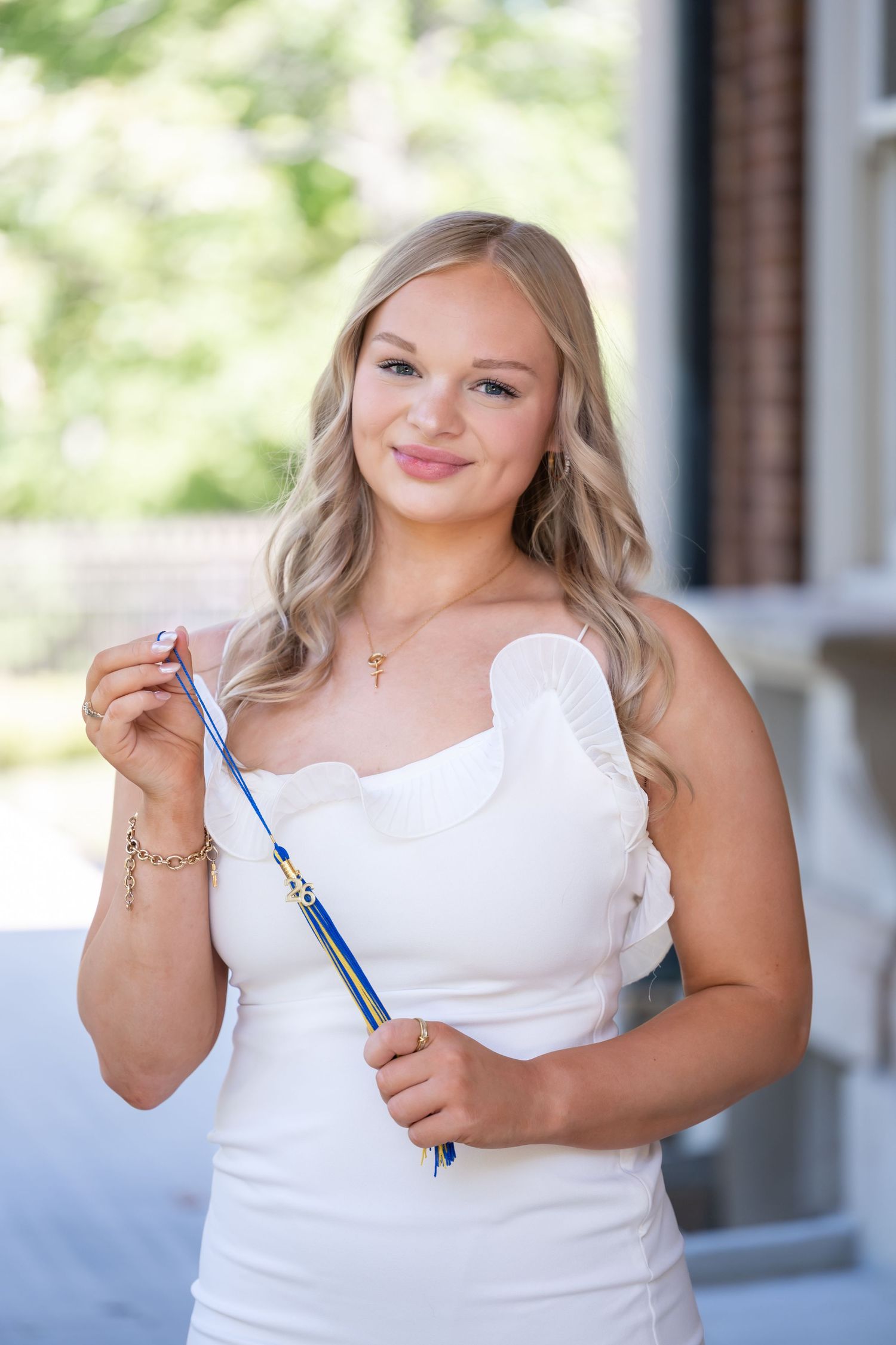 Young woman in white dress holding a blue baton, smiling outdoors for a senior portrait photo.
