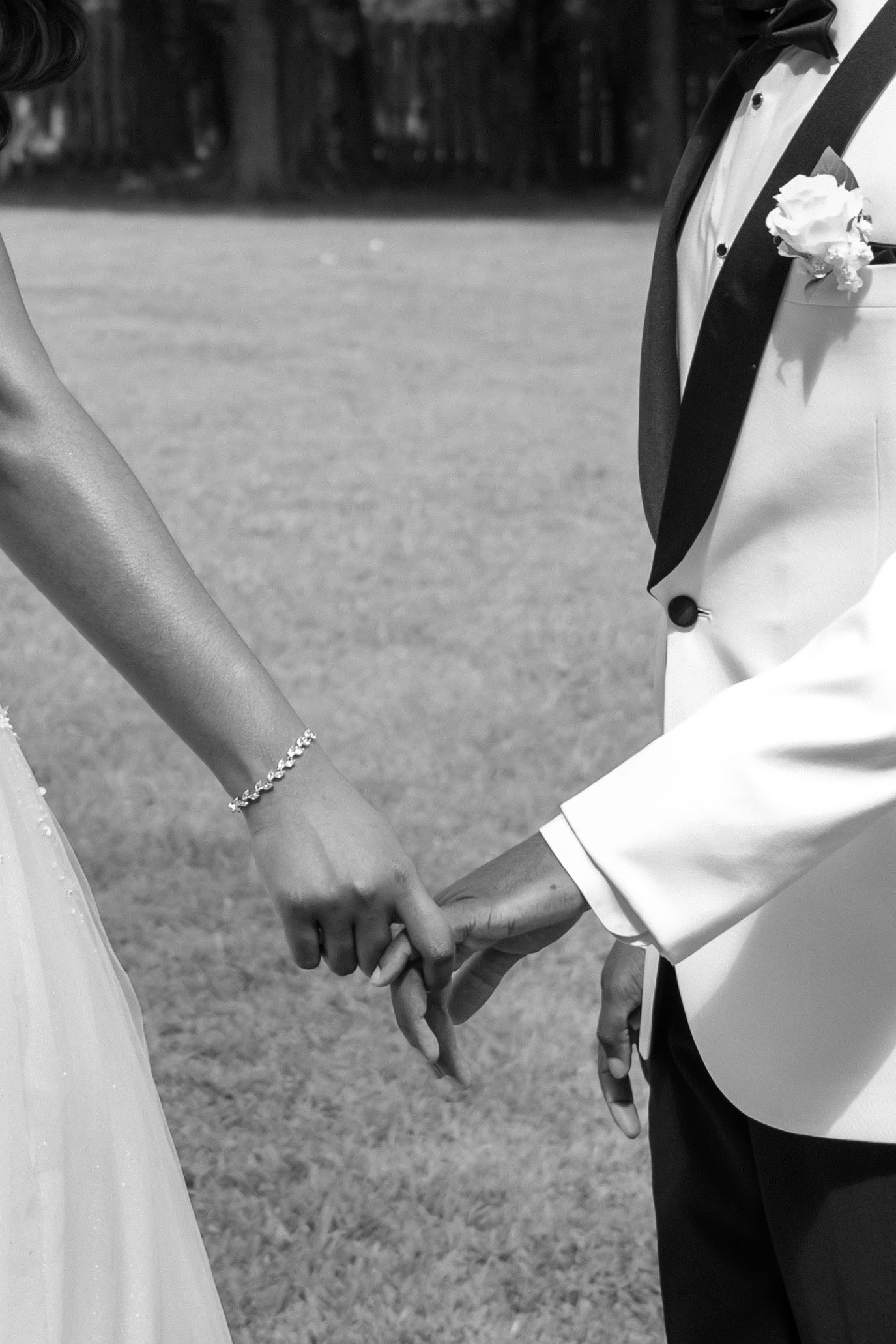 Black and white photo of a bride and groom holding hands at their outdoor wedding ceremony.
