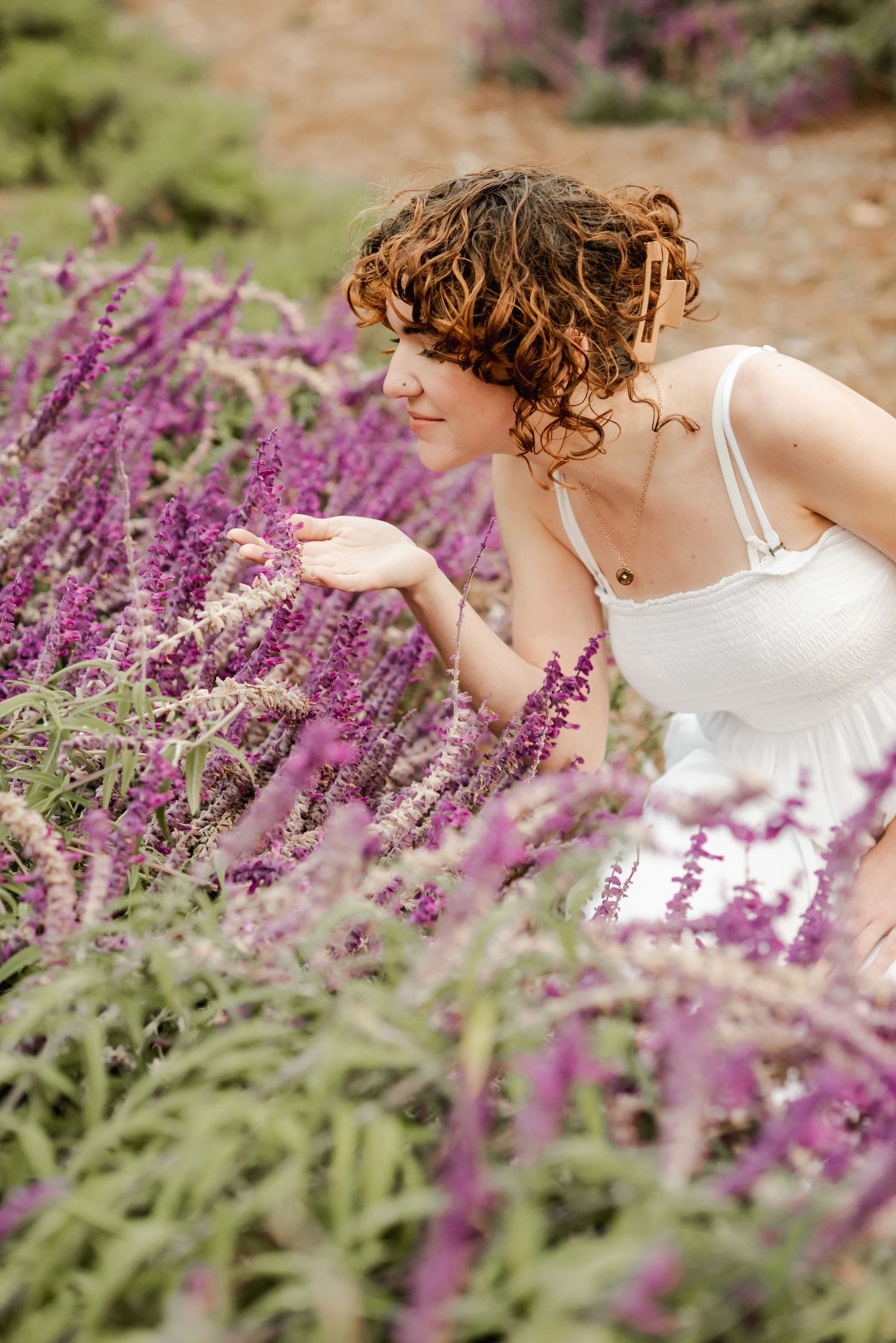 Woman in white dress leaning over vibrant purple lavender flowers in garden.
