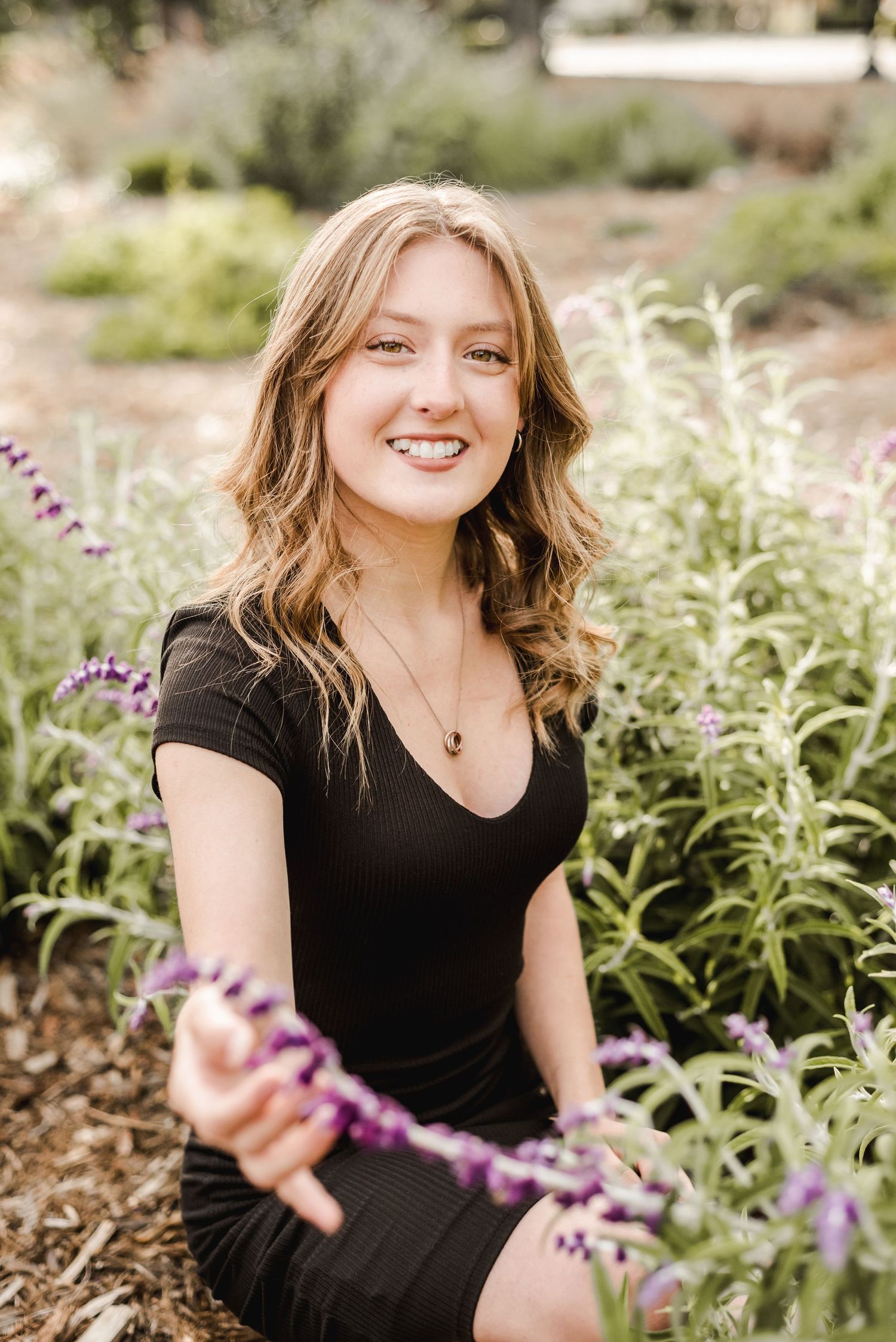 Senior portrait session in a garden with purple flowers and natural lighting.