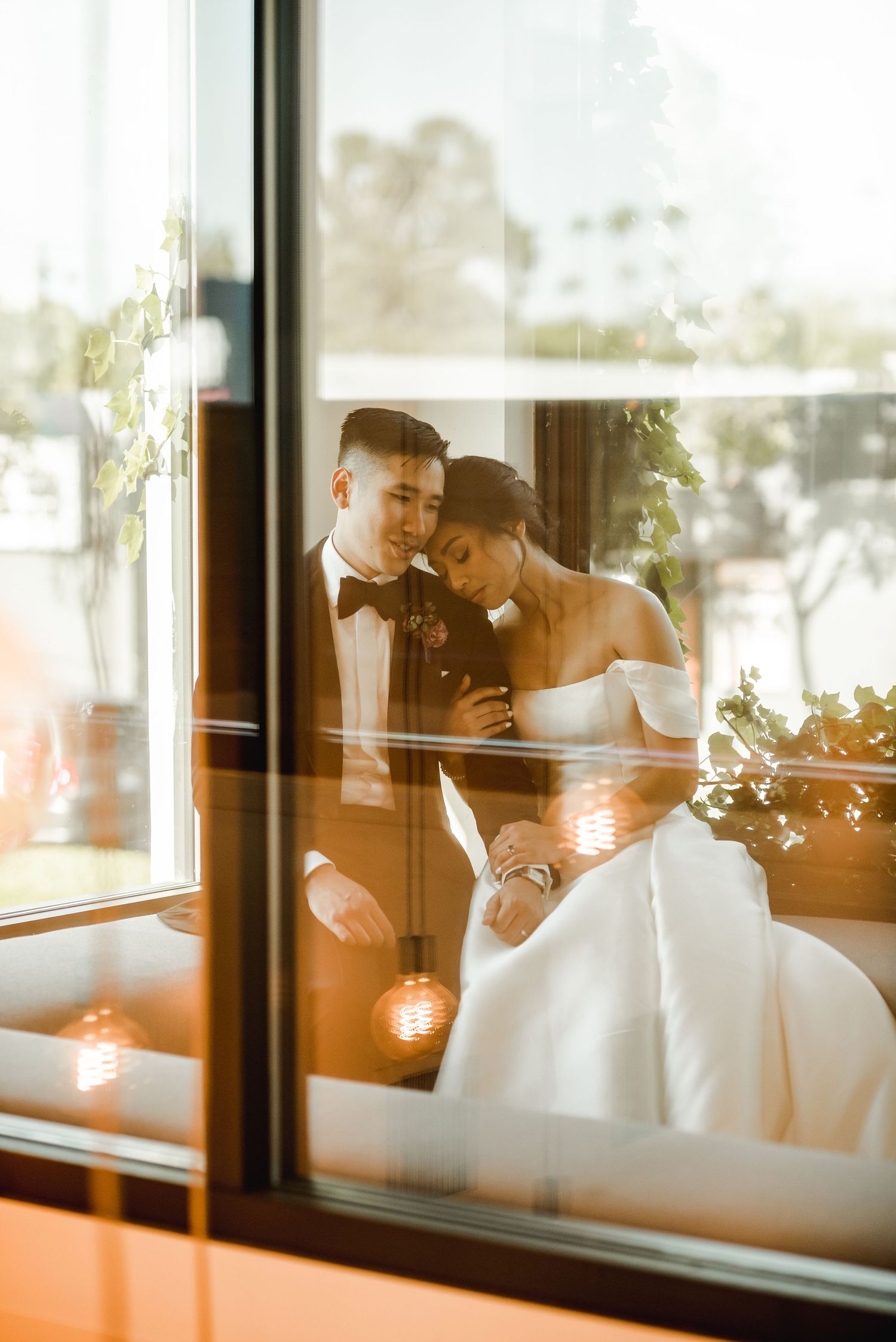 Romantic wedding couple embracing by window in warm sunset light.
