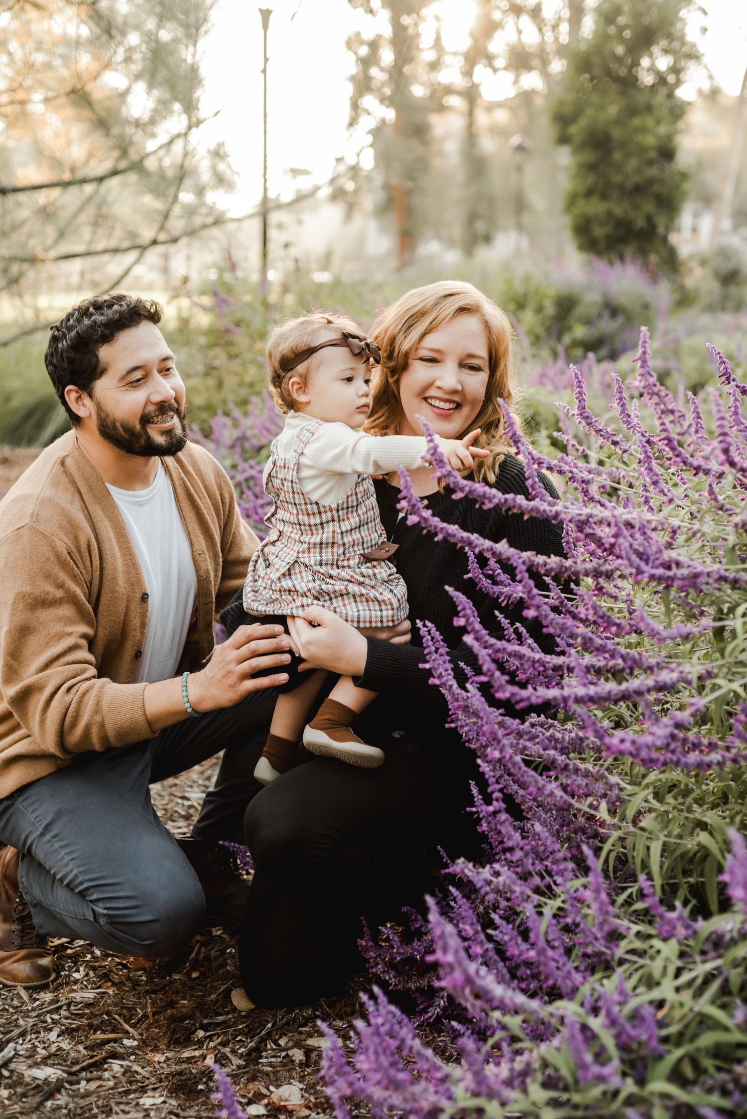 A family shares joyful moments among blooming purple flowers in a natural outdoor setting.