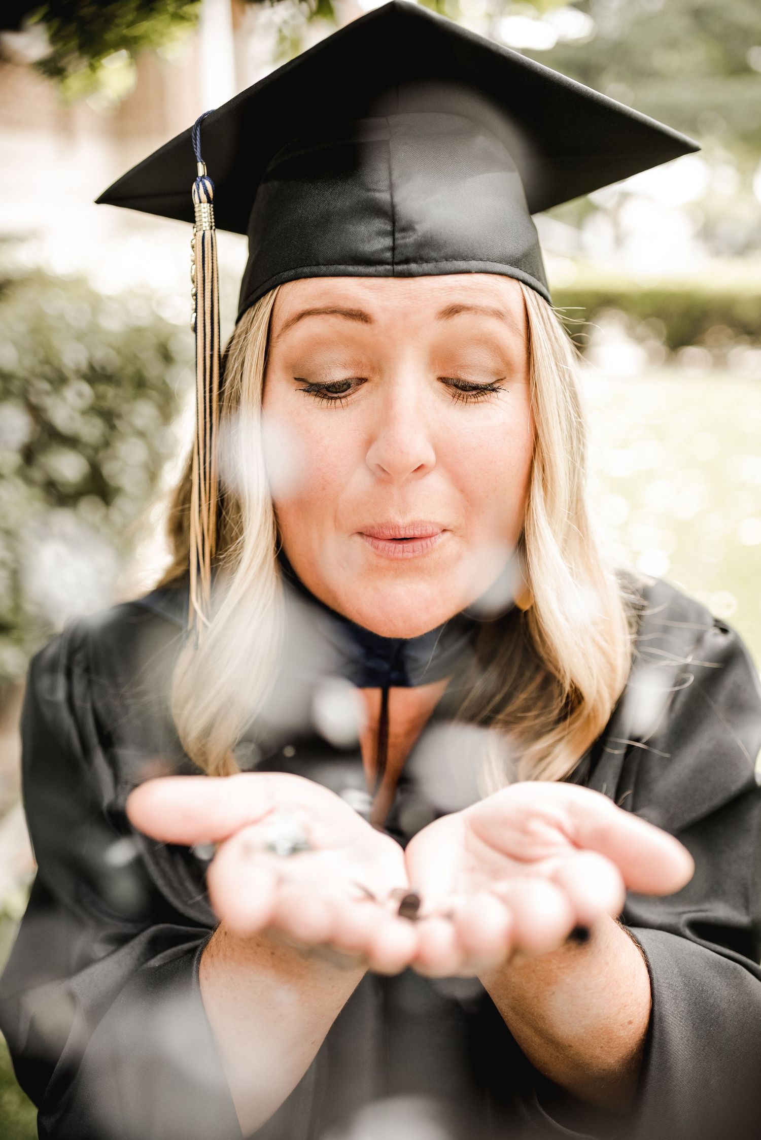 A graduate in cap and gown blows glitter from cupped hands in a joyful celebration photo.