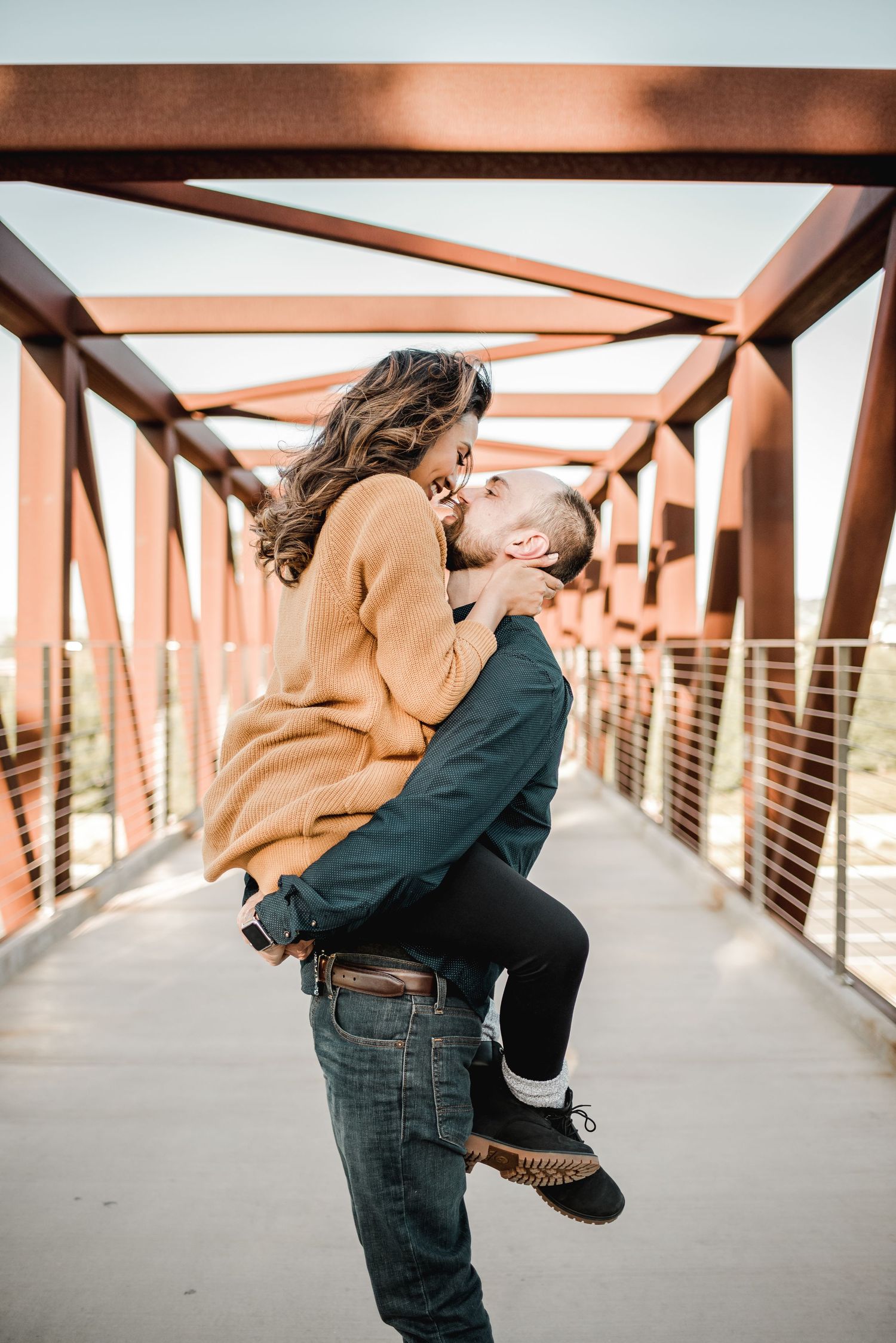 Playful couple sharing romantic moment on modern bridge during sunset.