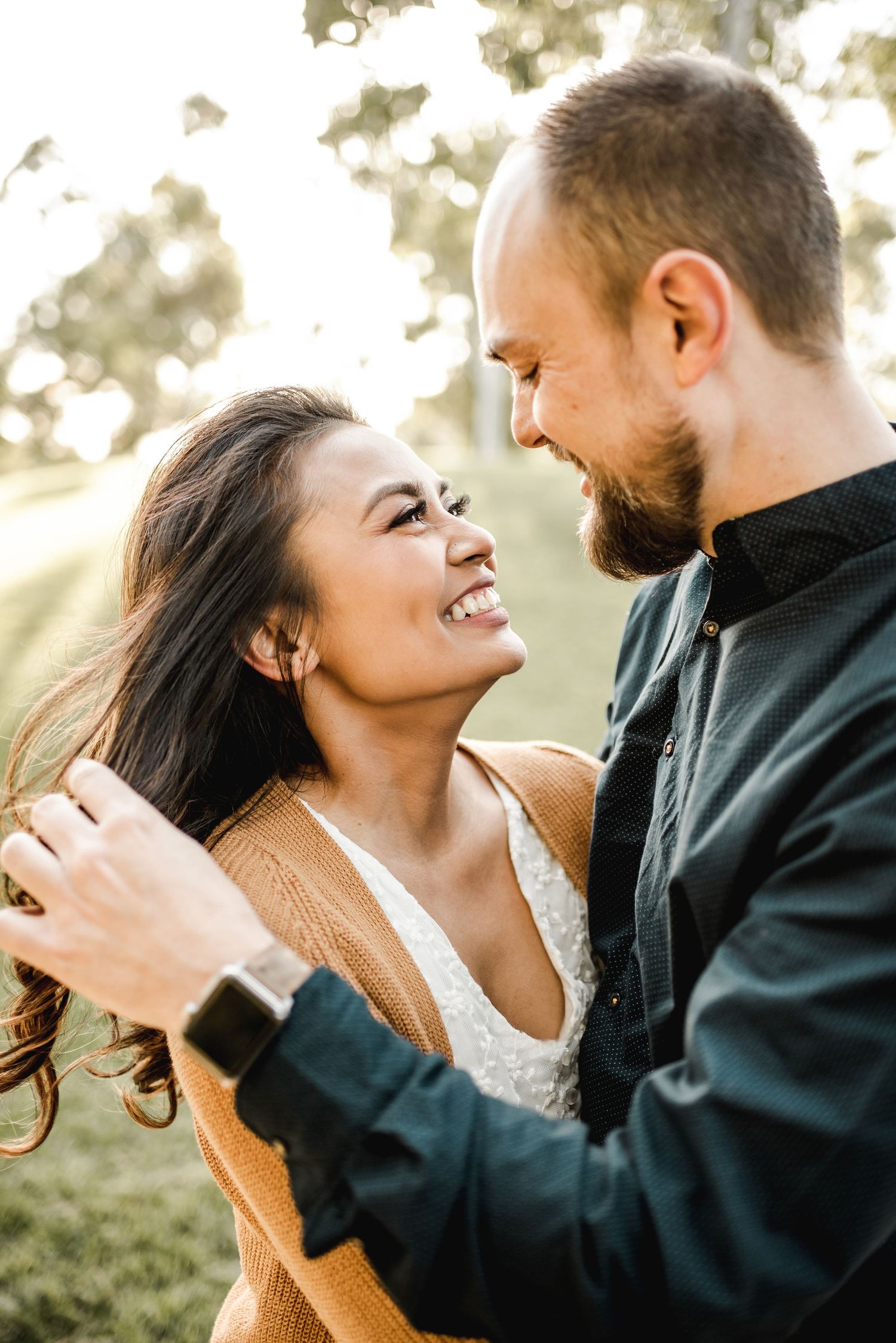 A romantic couple laughs together during a sunset photoshoot in a natural outdoor setting.