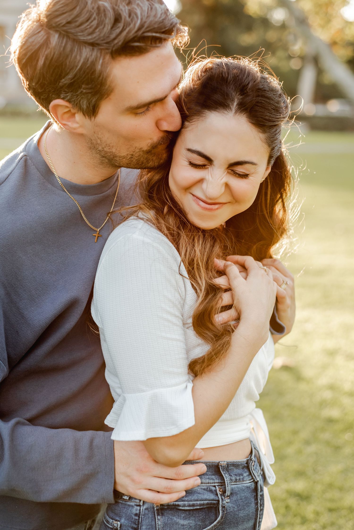 Intimate couple embracing in casual outfits during golden hour outdoor photoshoot.