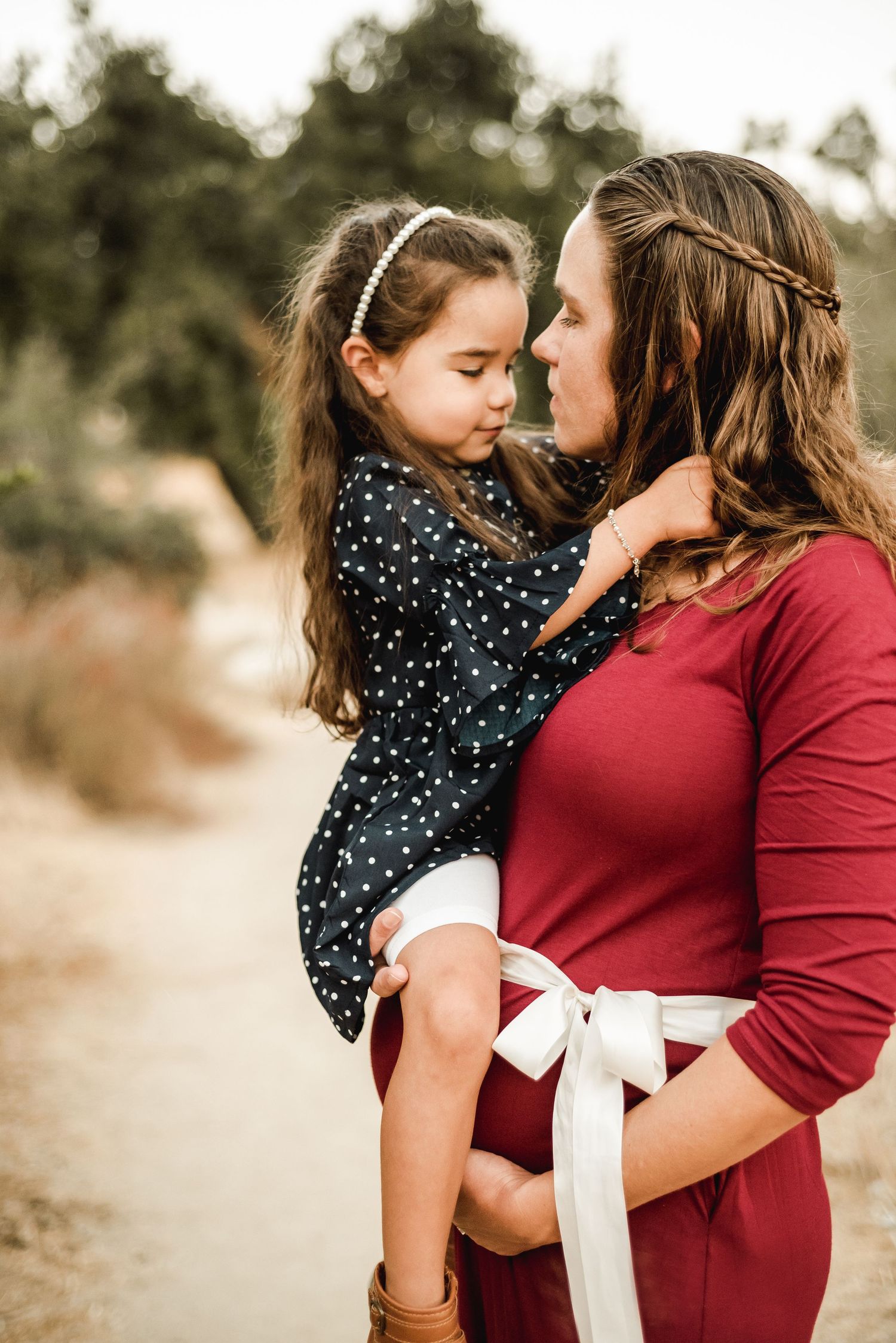 A mother and daughter share tender moments in matching burgundy and polka dot outfits against a natural backdrop.