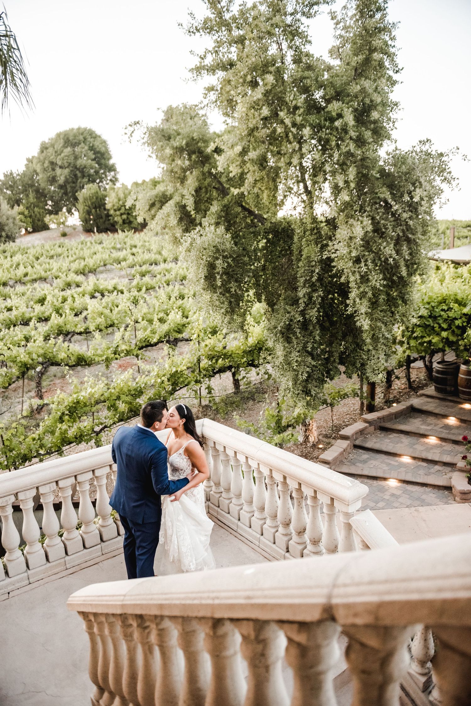 A couple shares a moment on an elegant stone balcony overlooking vineyard grounds.