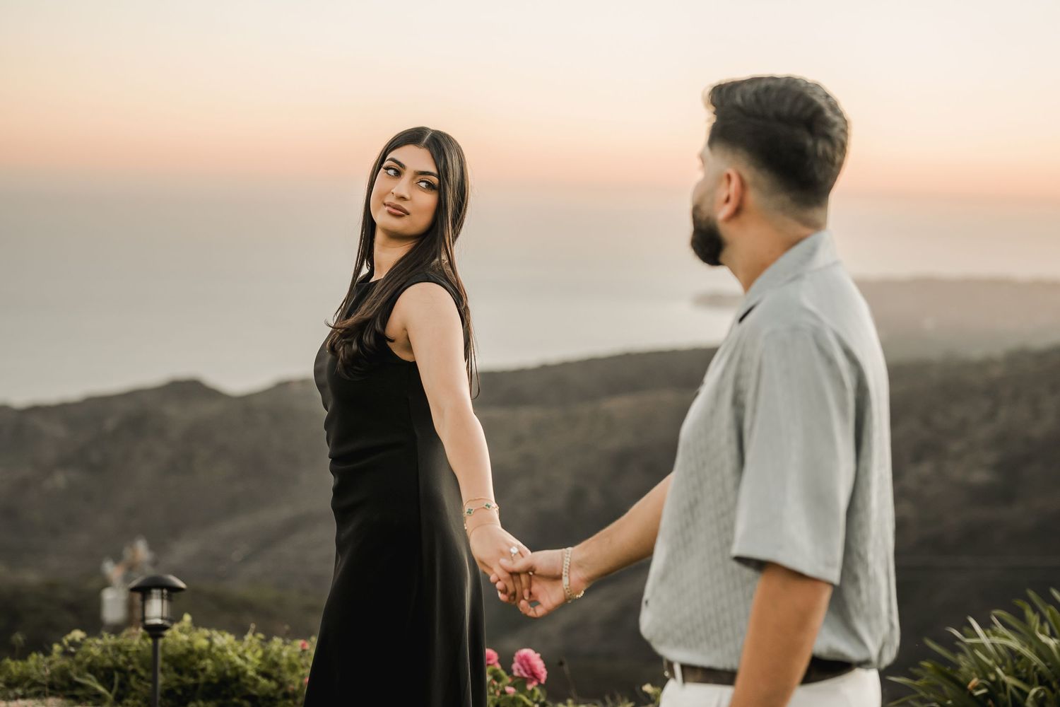 Romantic couple holding hands against scenic mountain backdrop during golden hour.