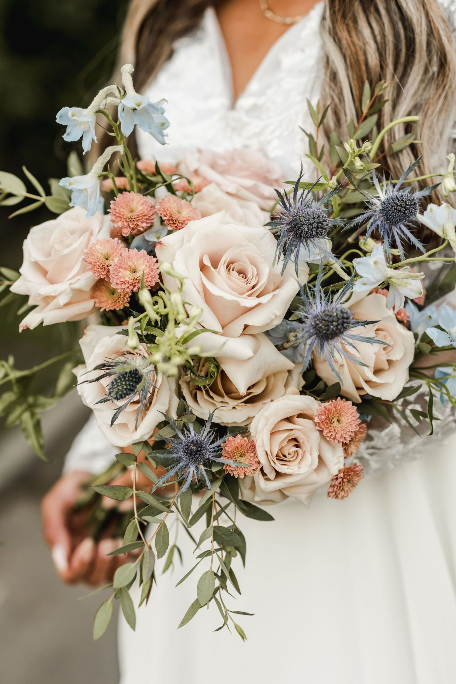 Bridal bouquet with blush roses, blue thistles, and eucalyptus leaves.