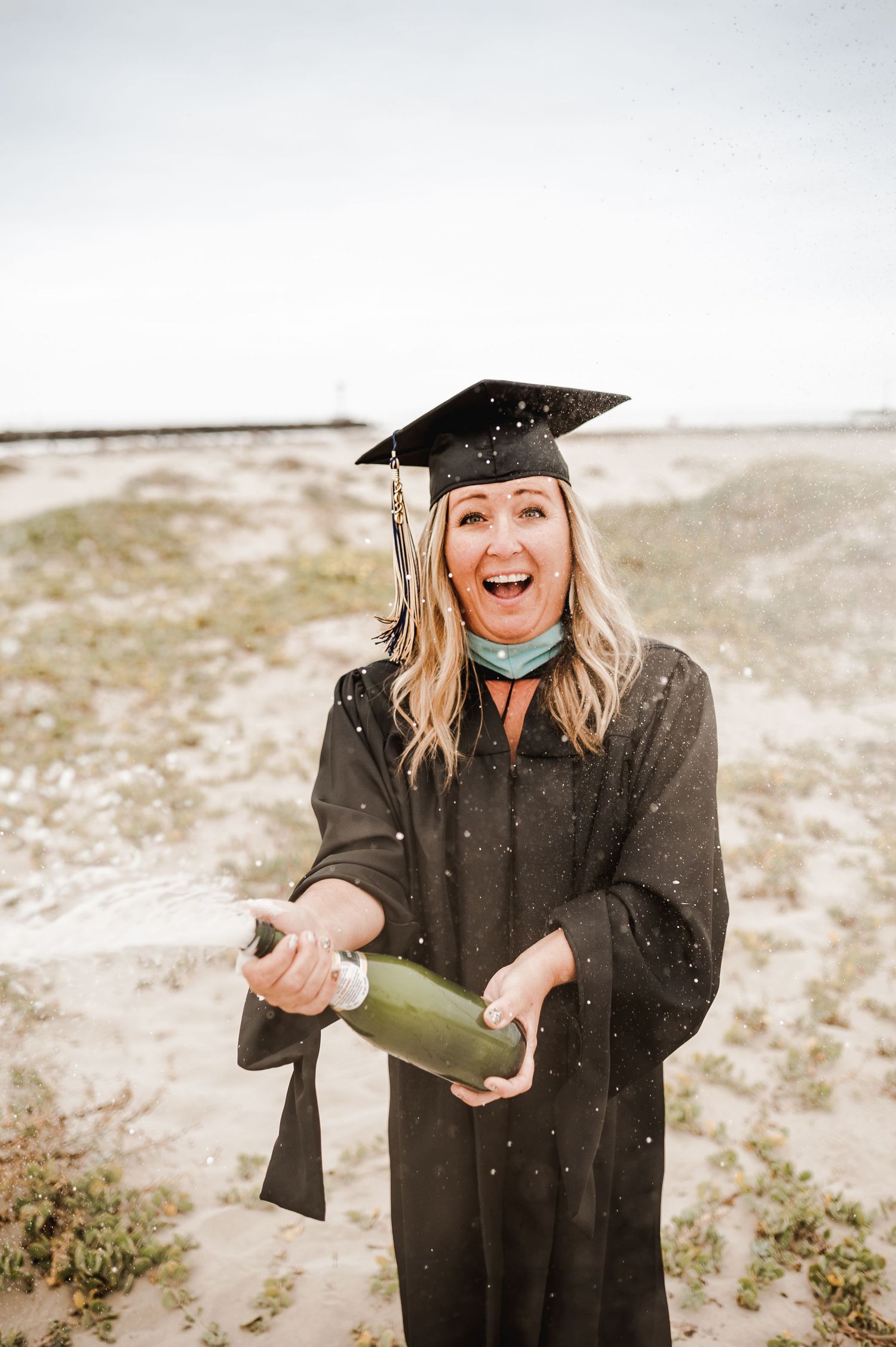 A graduate in cap and gown celebrates with champagne during an outdoor photoshoot.
