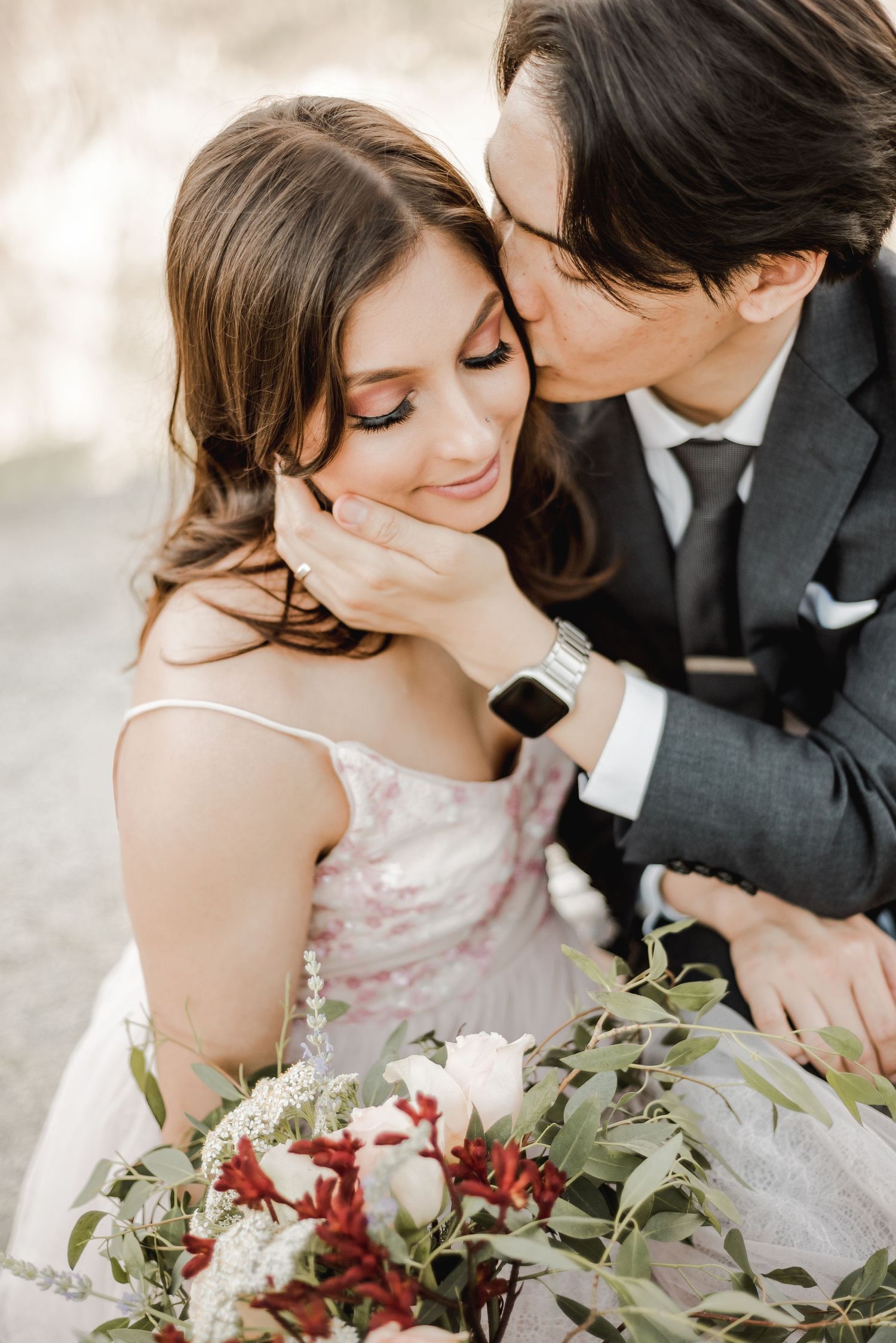 A tender moment between a couple with a beautiful bouquet of red and white flowers.
