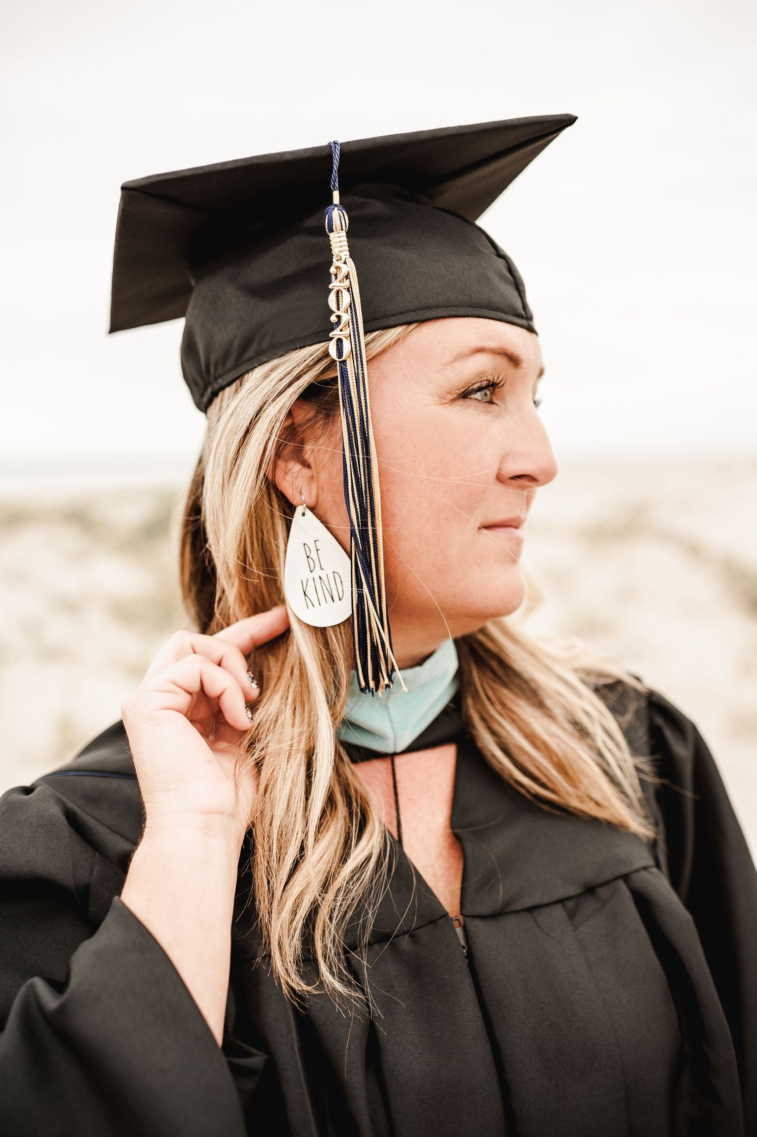 A graduate in traditional black cap and gown poses thoughtfully against a neutral background.