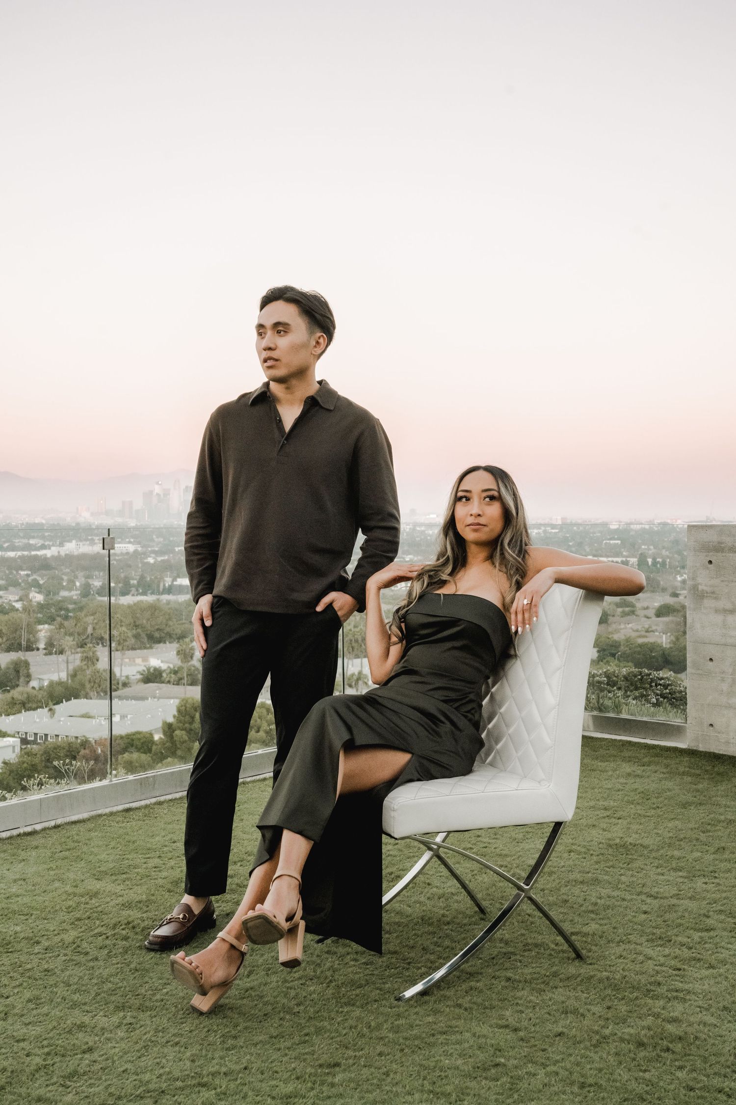 Stylish couple posing on rooftop terrace with cityscape view at sunset.