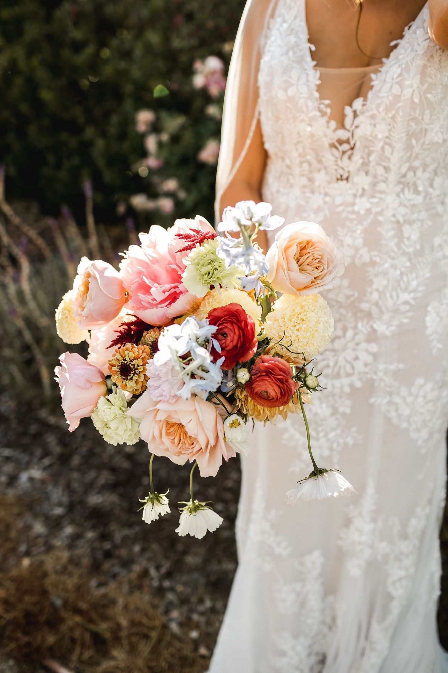 A detailed shot of a bridal bouquet featuring pink and peach roses against a lace wedding dress.