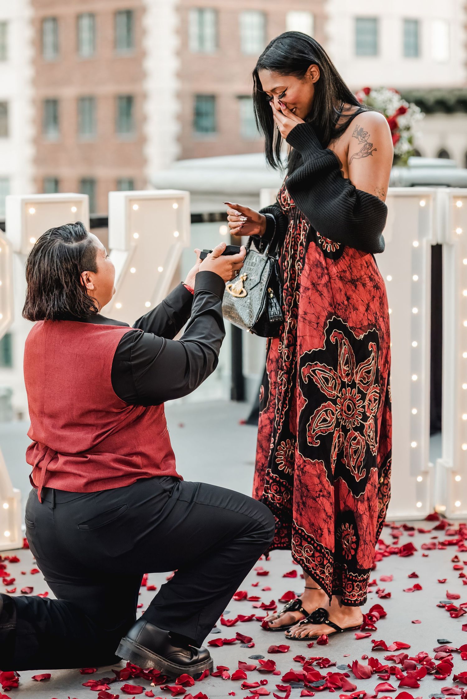 A romantic rooftop proposal with rose petals scattered on the ground.