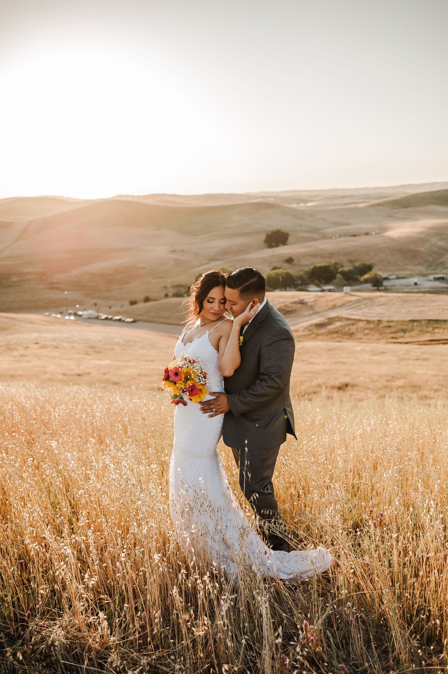 Romantic wedding couple embracing in a sun-drenched field during golden hour.