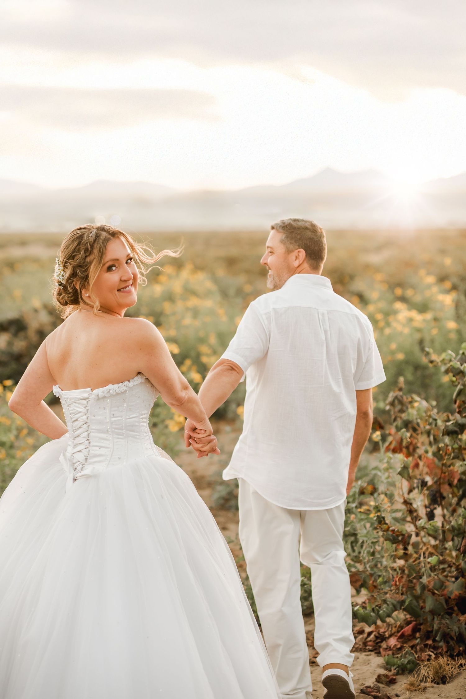 A romantic wedding photo of a couple walking hand in hand through a vineyard at sunset.