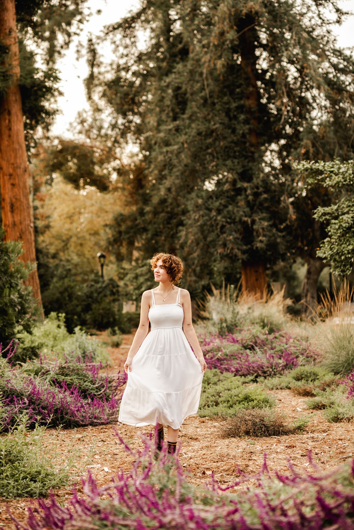 A white sundress flows gracefully among purple wildflowers in a serene garden setting at golden hour.