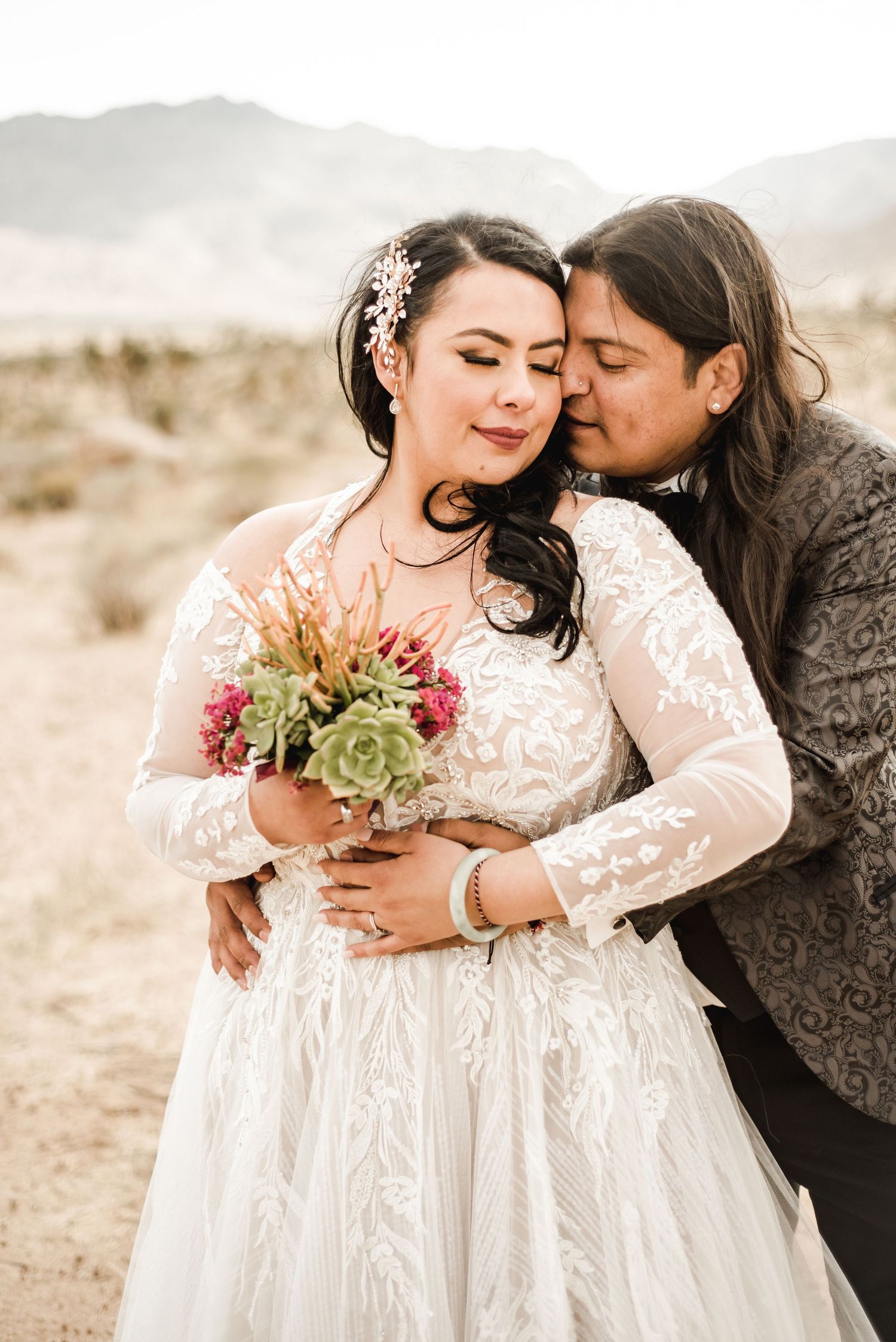 Intimate wedding portraits in white lace dresses against a desert landscape.