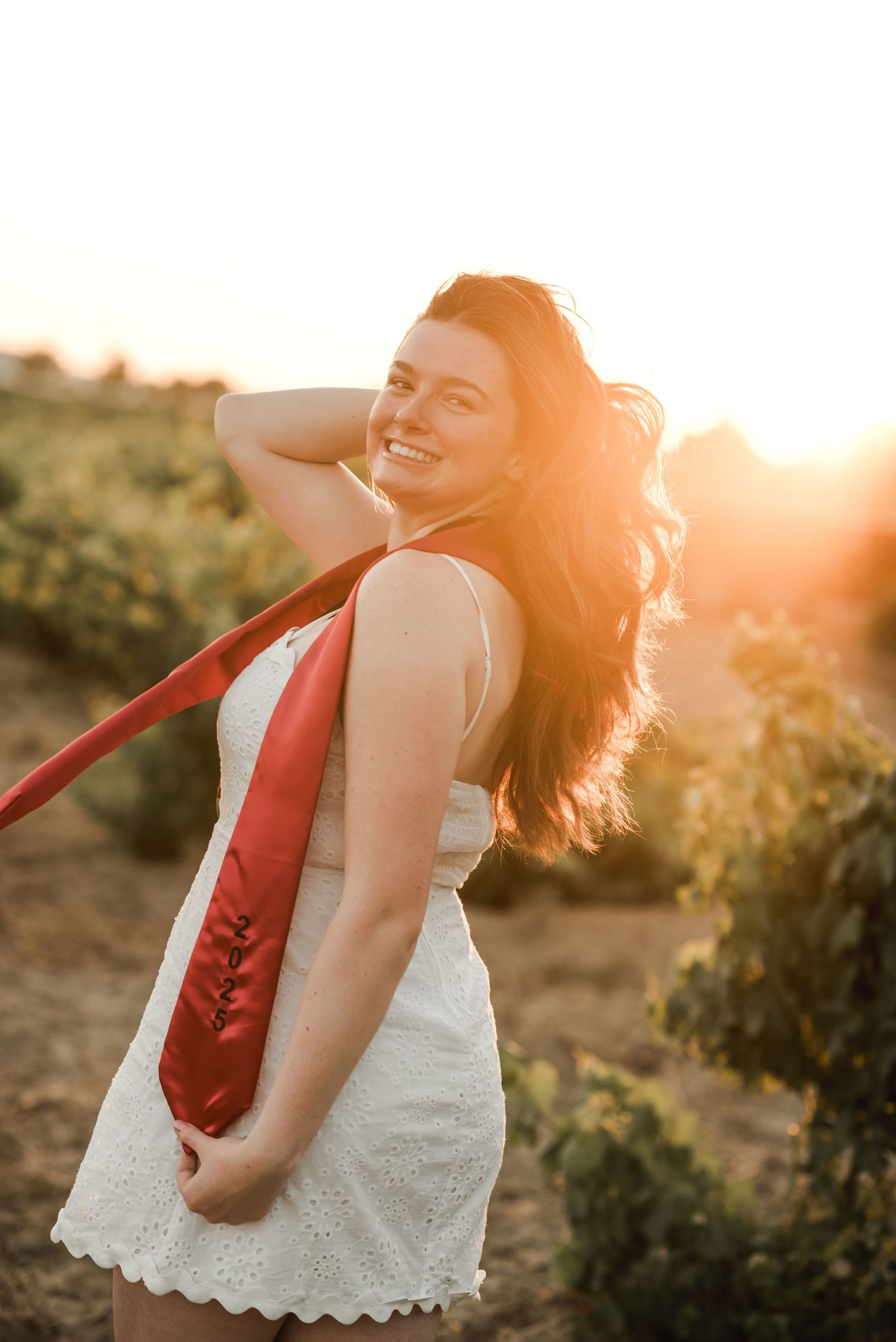 Person in white dress twirling against sunset in a vineyard setting.