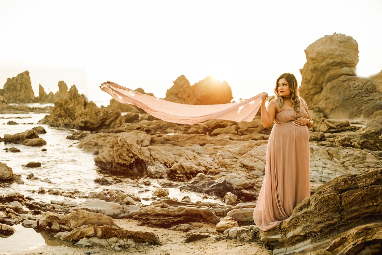 A romantic sunset photoshoot on a rocky beach with golden light and crashing waves.