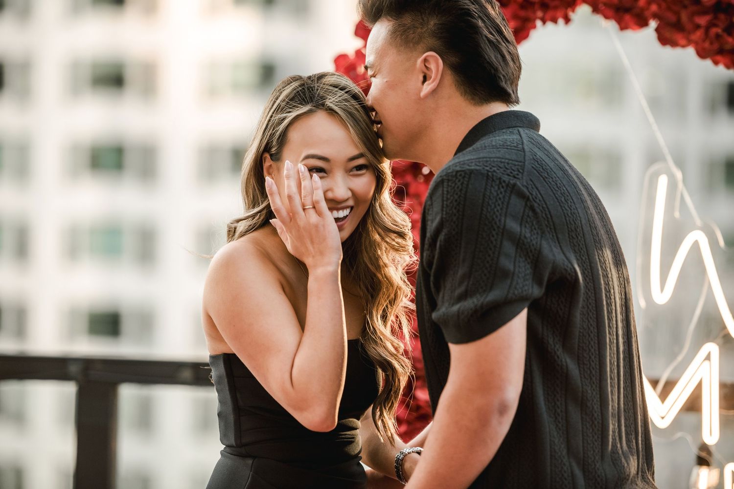 A joyful moment captured during a rooftop proposal with a decorative red heart arch.