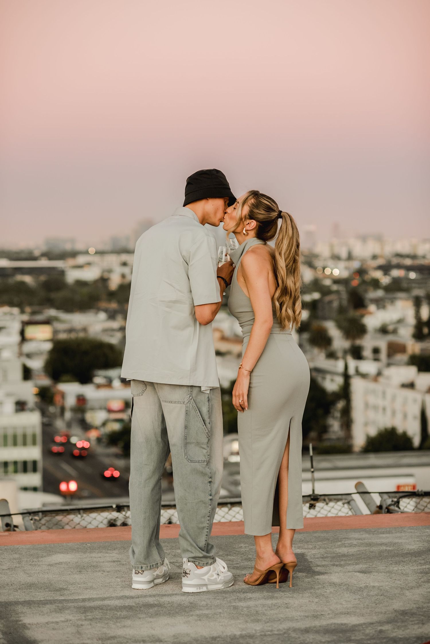 Couple in matching grey outfits sharing intimate moment on urban rooftop at sunset.
