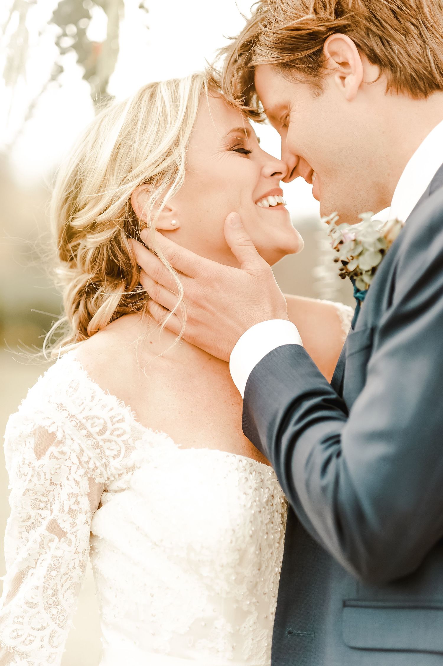 Romantic wedding portrait of couple in formal attire touching foreheads in warm sunlight.