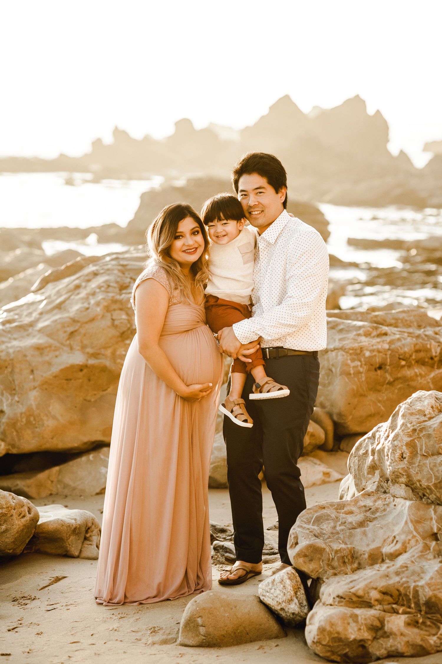 A family poses together on coastal rocks during golden hour at the beach.
