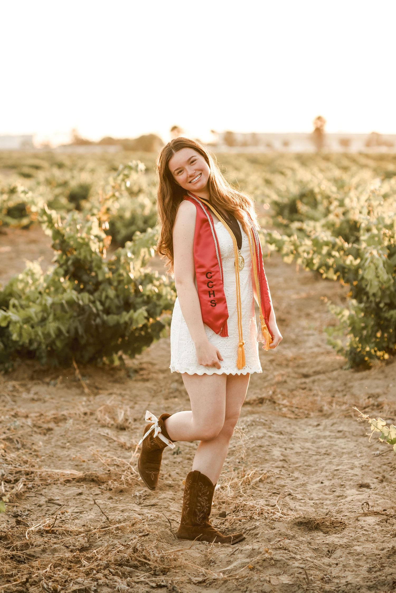 Person in white dress and red vest dancing in a sunny vineyard.