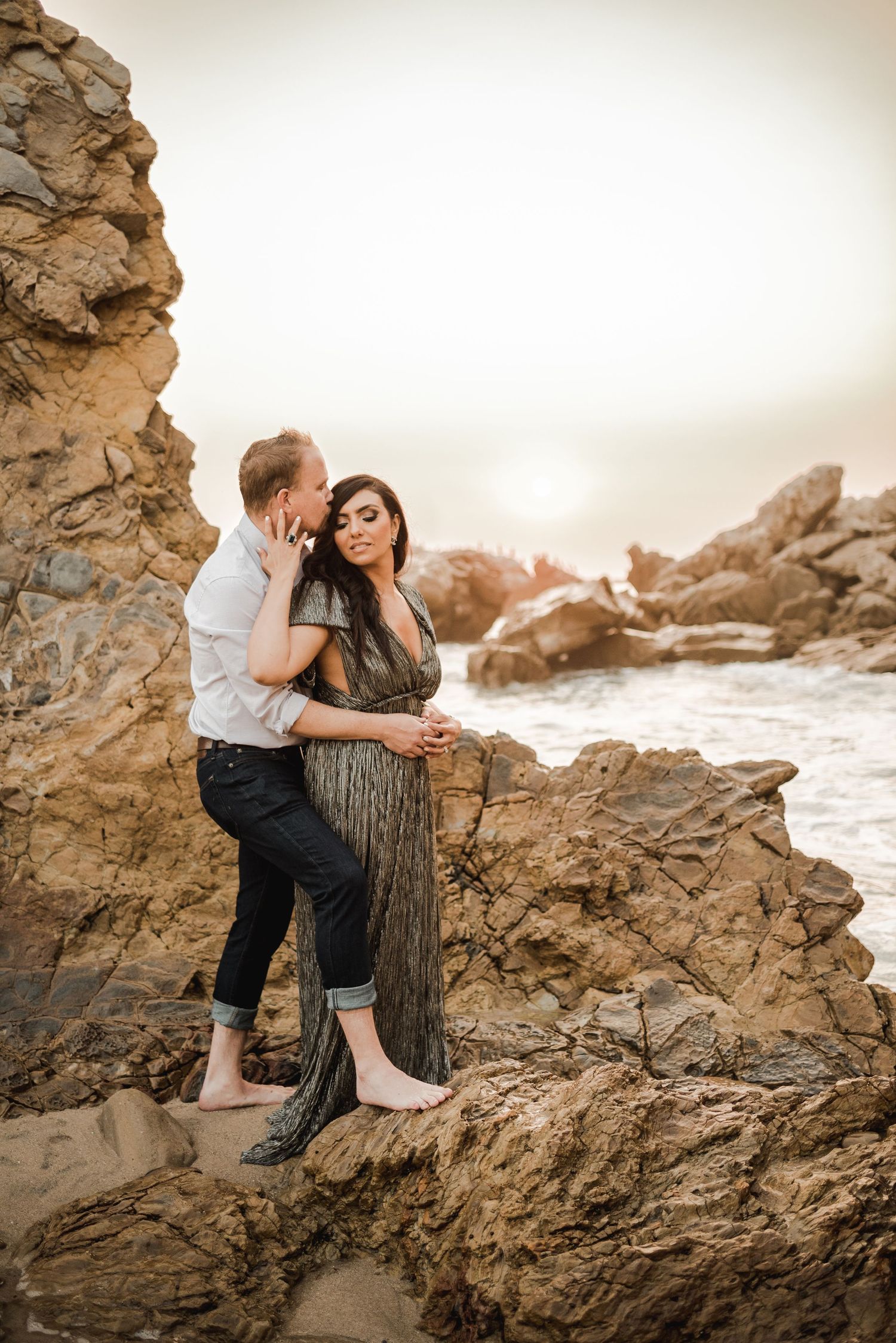 Couple sharing intimate moments on coastal rocks during sunset.