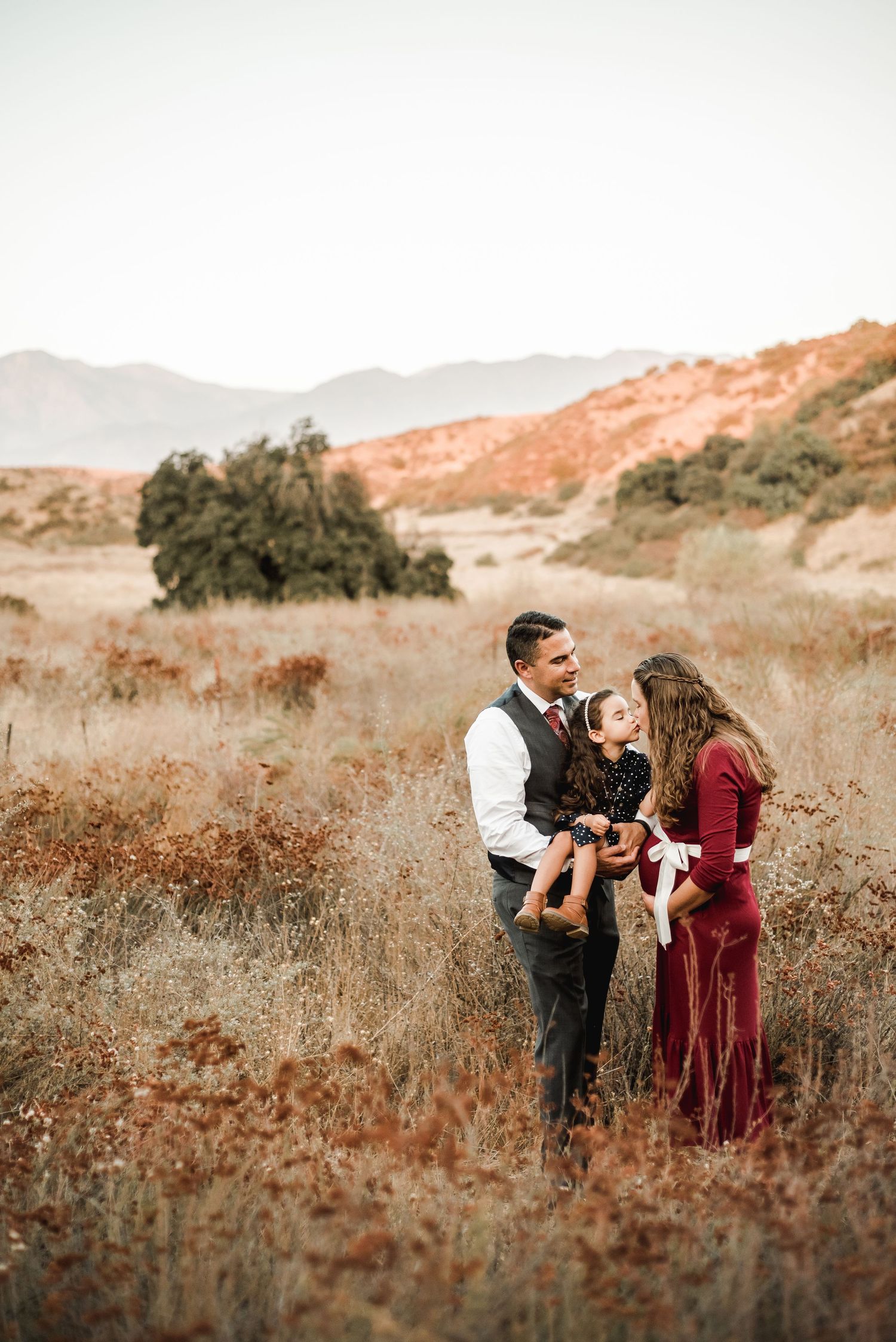 A family photoshoot in a golden field with mountains visible in the background at sunset.