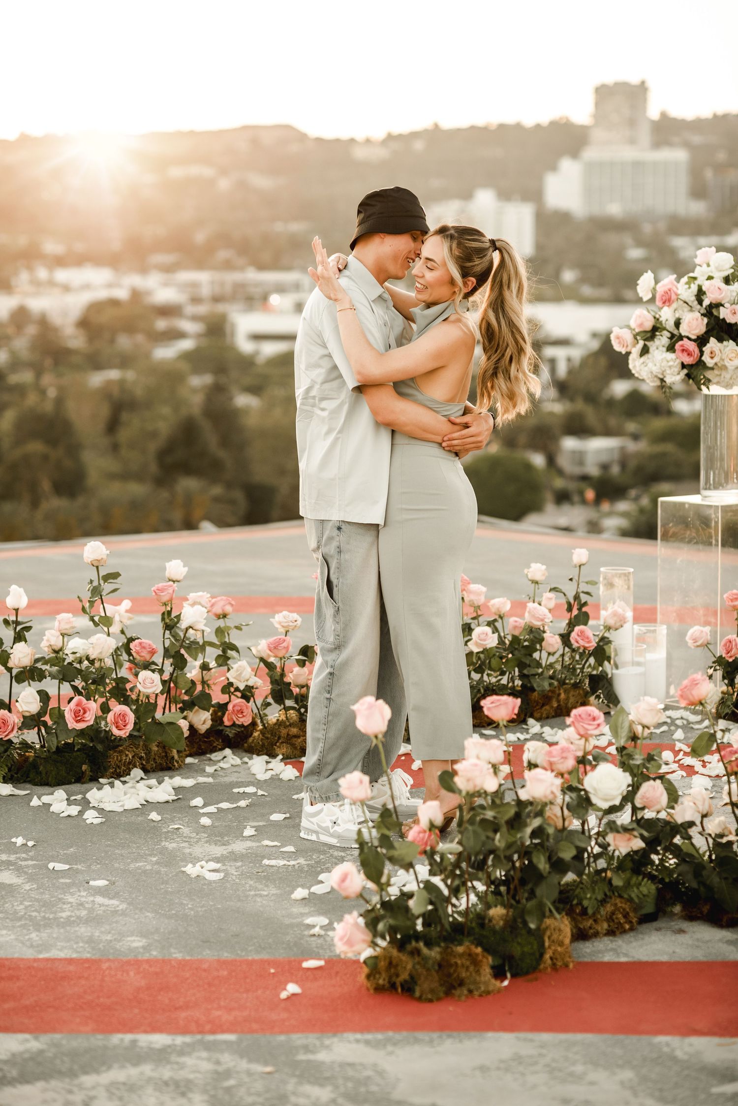 Romantic rooftop proposal scene with pink roses and city view at golden hour.